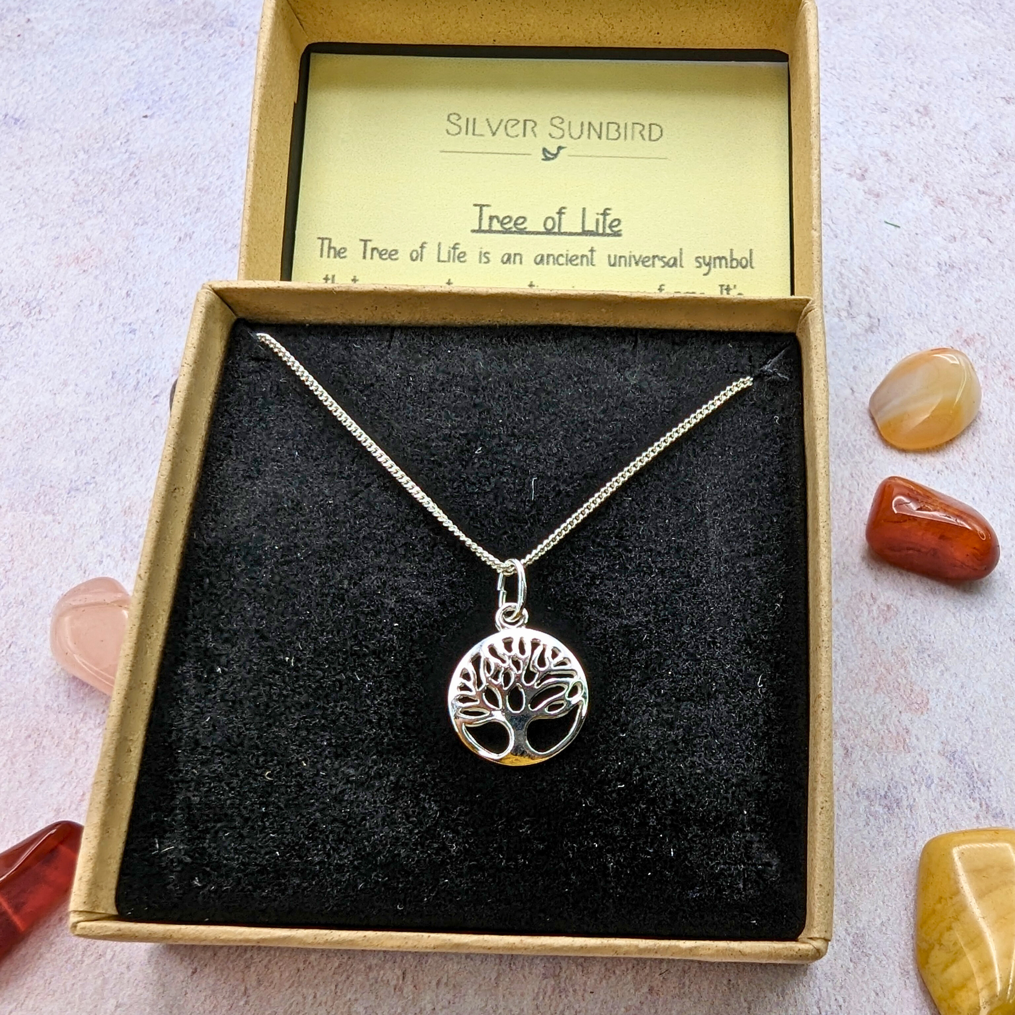 The Silver Sunbird Tree of Life Sterling Silver Necklace comes in a black velvet box with a meaning card, beautifully accented by polished brown, white, and orange stones—a meaningful and elegant jewelry piece.