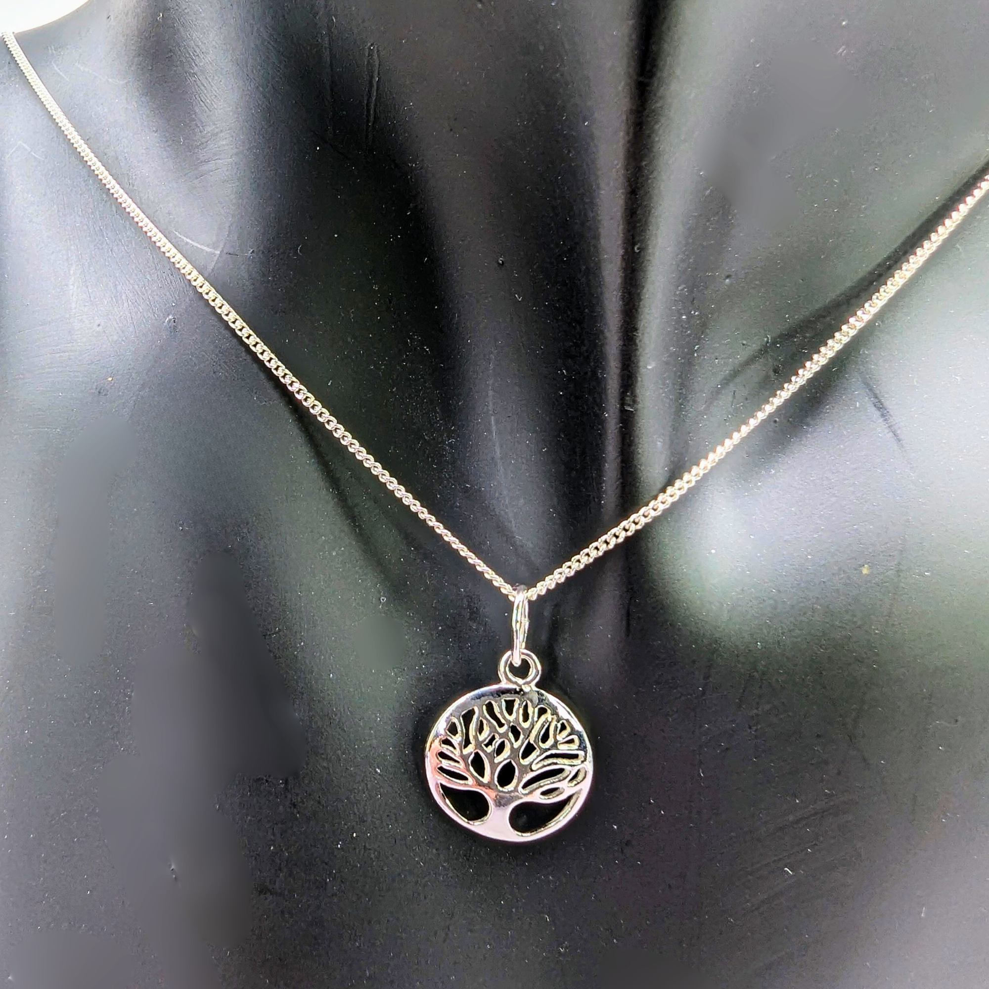 The Silver Sunbird Tree of Life Sterling Silver Necklace, featuring a circular pendant with a cut-out tree design, is displayed on a black mannequin bust as a meaningful jewelry piece.