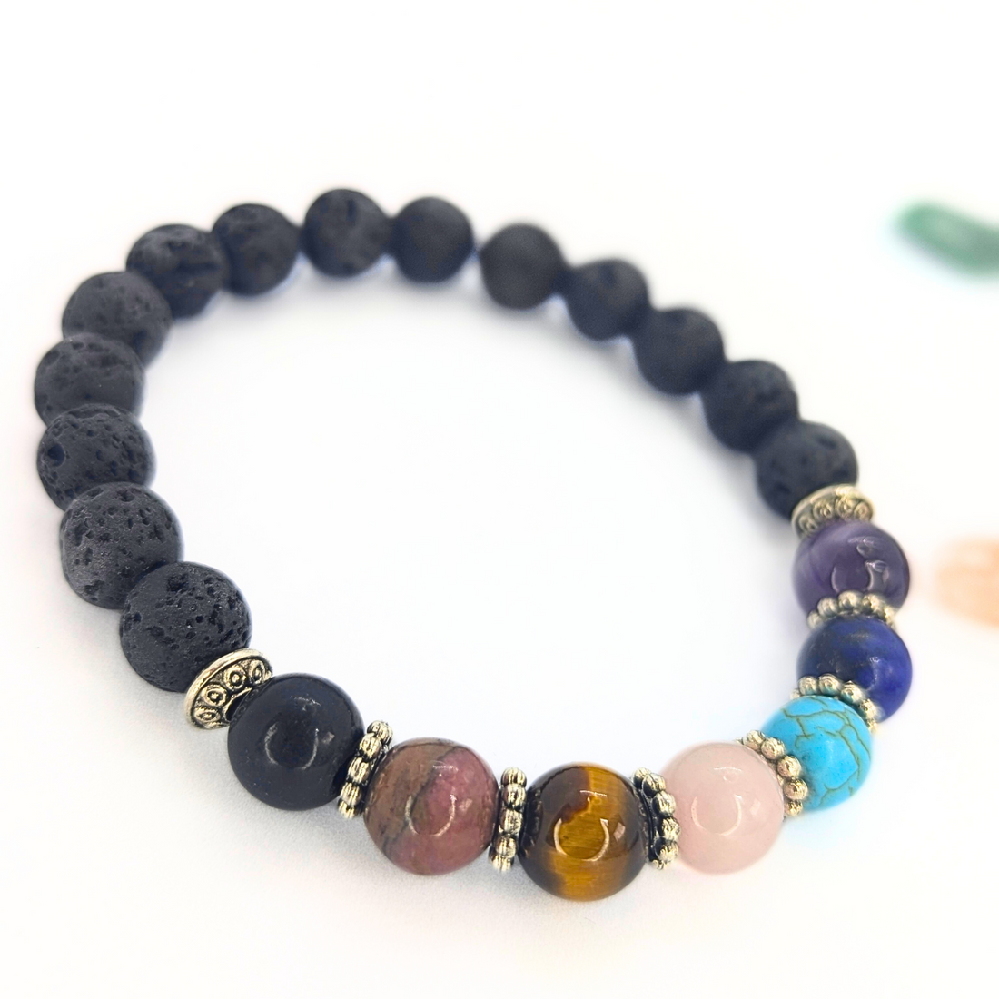 The Chakra Bracelet by Silver Sunbird features black lava stones and colorful semi-precious gemstones with silver spacers—ideal for wearing as a chakra bracelet or for diffusing essential oils. Displayed on a white background.