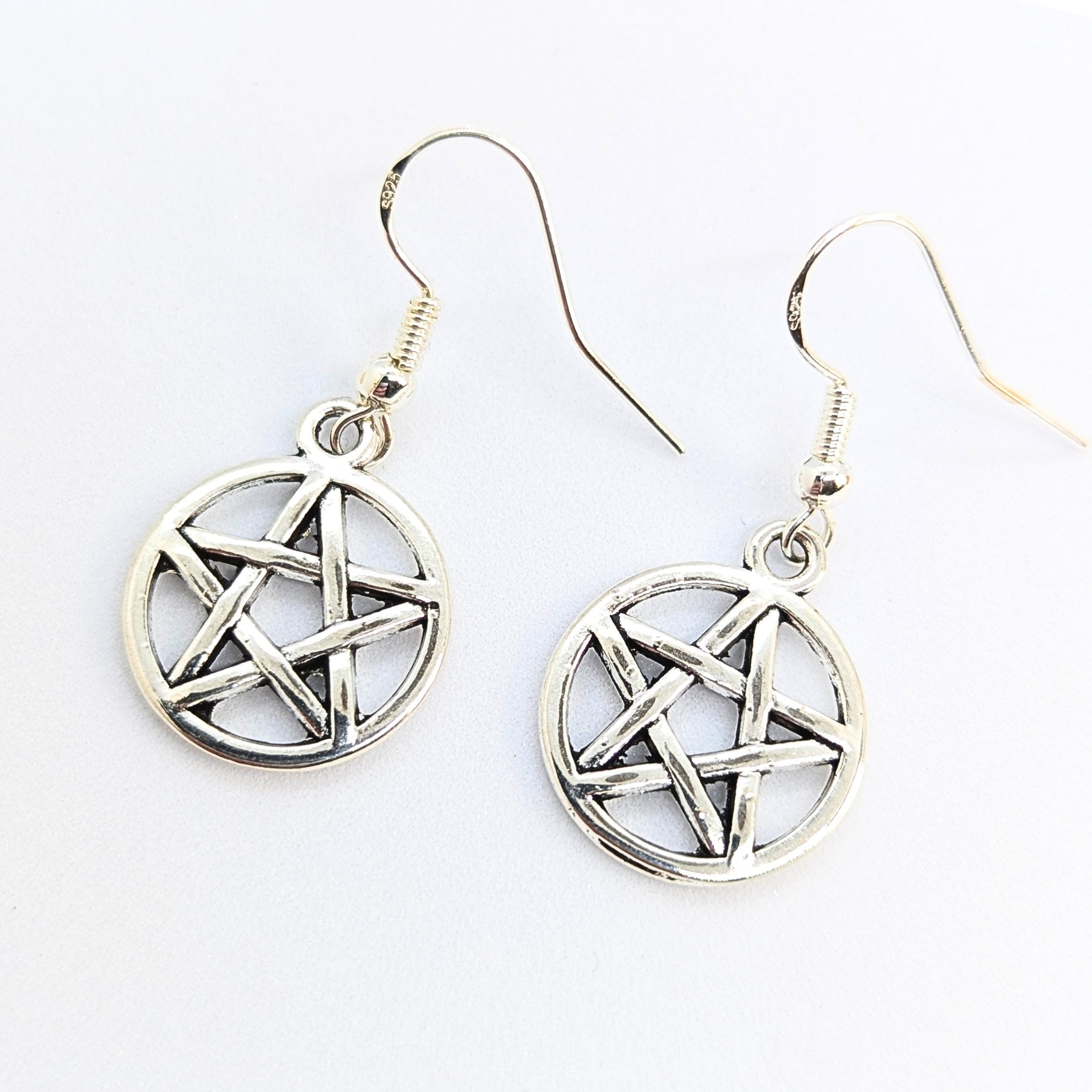 The Silver Sunbird Pentagram Earrings are sterling silver dangle earrings with round pentagram charms, subtly showcasing pagan symbolism.