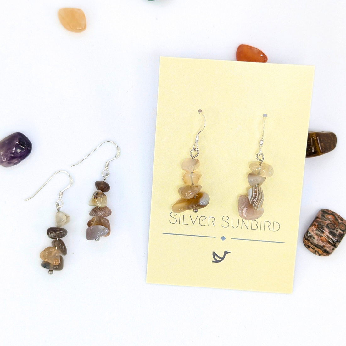 A pair of handmade Botswana Agate Gemstone Earrings by Silver Sunbird on a branded card, with a matching loose pair beside it. Polished stones in various colors add flair—perfect for Sterling silver earring lovers.