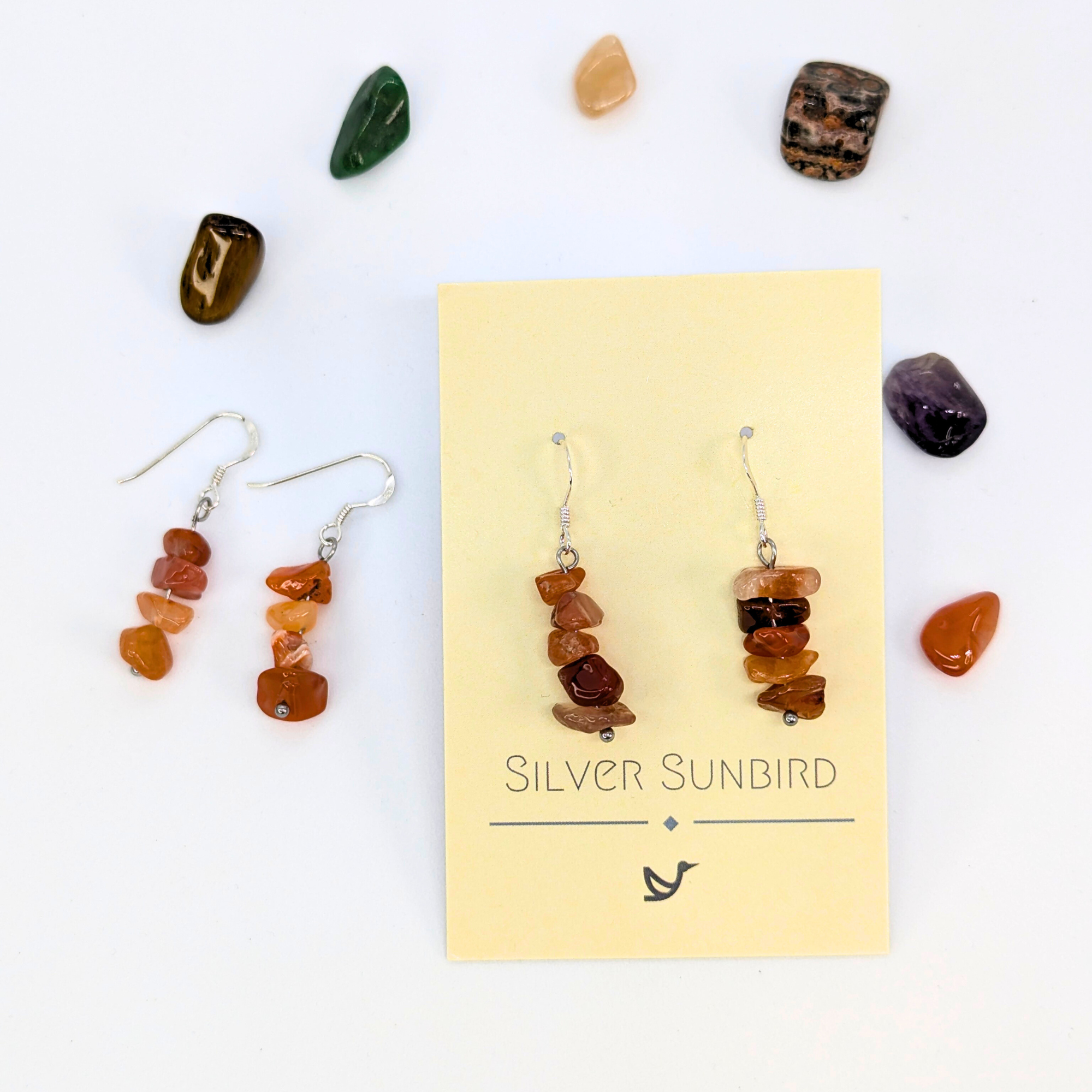 Carnelian Agate Earrings by Silver Sunbird: handmade sterling silver dangle earrings with stacked brown stones, displayed on a branded card and surrounded by polished gemstones—a unique accessory for any occasion.