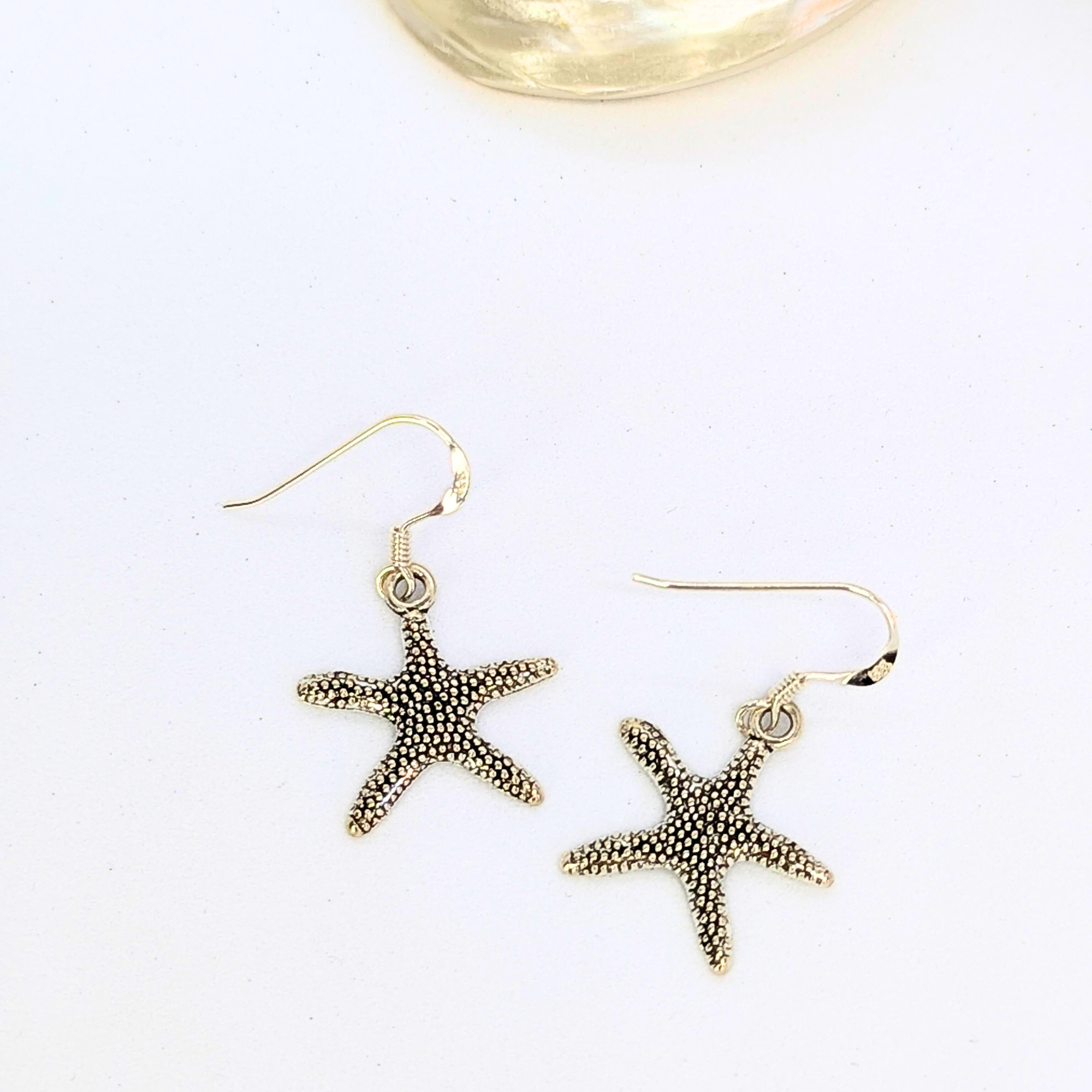 Silver Sunbird’s Detailed Silver Starfish Earrings feature a textured design, perfect for boho jewelry lovers. These sterling silver earrings dangle elegantly and are shown on a white background.