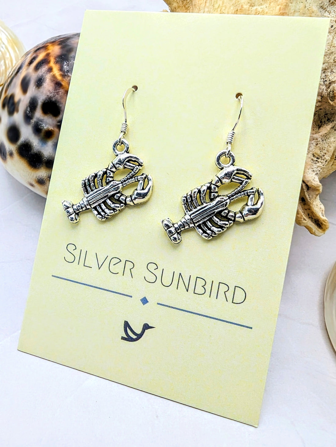 The Lively Lobster Earrings, by Silver Sunbird, are hypoallergenic and feature a nautical theme with a seashell backdrop to enhance your ocean spirit.