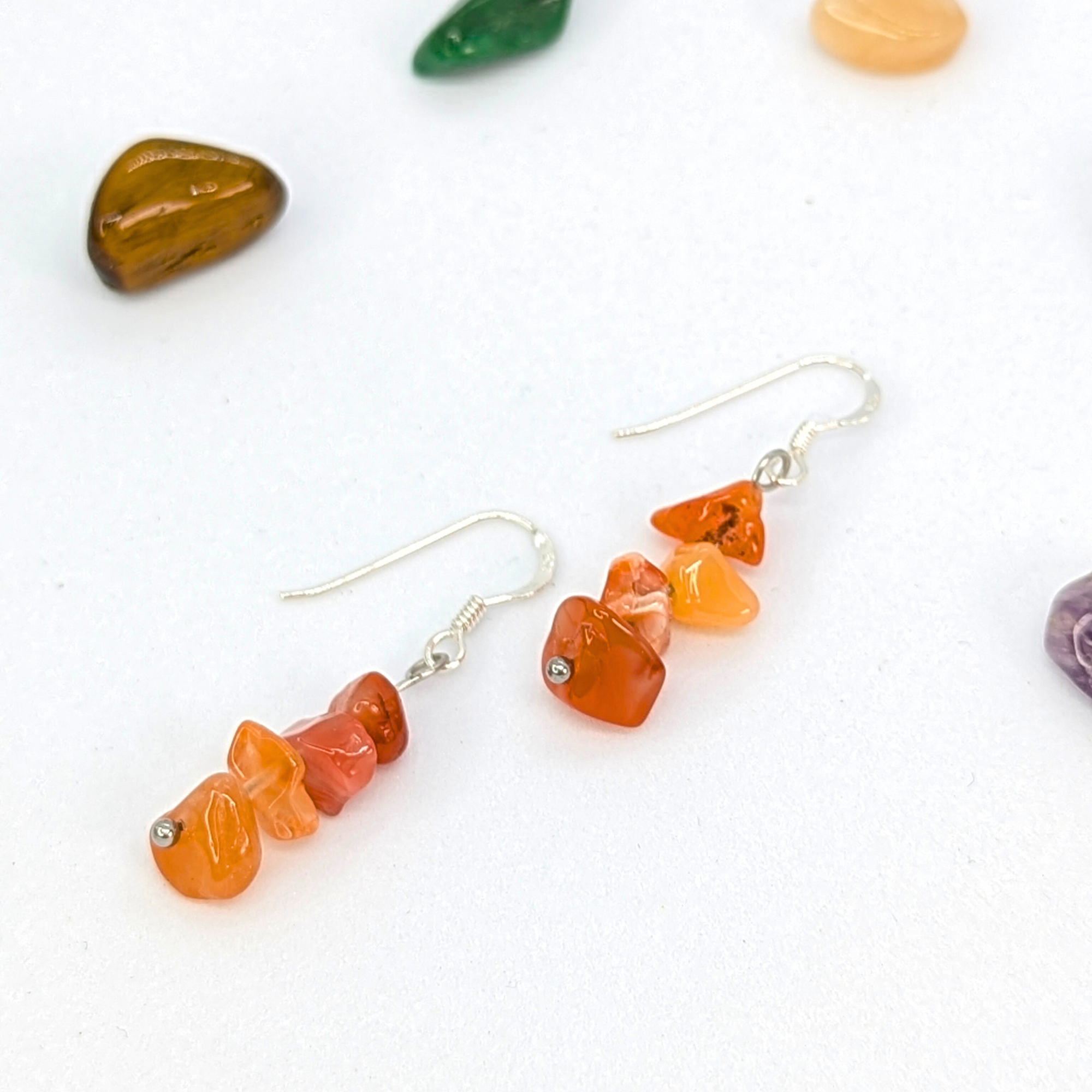 Carnelian Agate Earrings by Silver Sunbird feature handmade stacked orange and red gemstone chips on sterling silver dangle hooks, shown on a white surface with polished stones—perfect for lovers of vibrant, artisan jewelry.