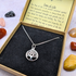 The Silver Sunbird Tree of Life Sterling Silver Necklace is shown in a brown box with black velvet lining and a symbolism card, with colorful stones scattered around.