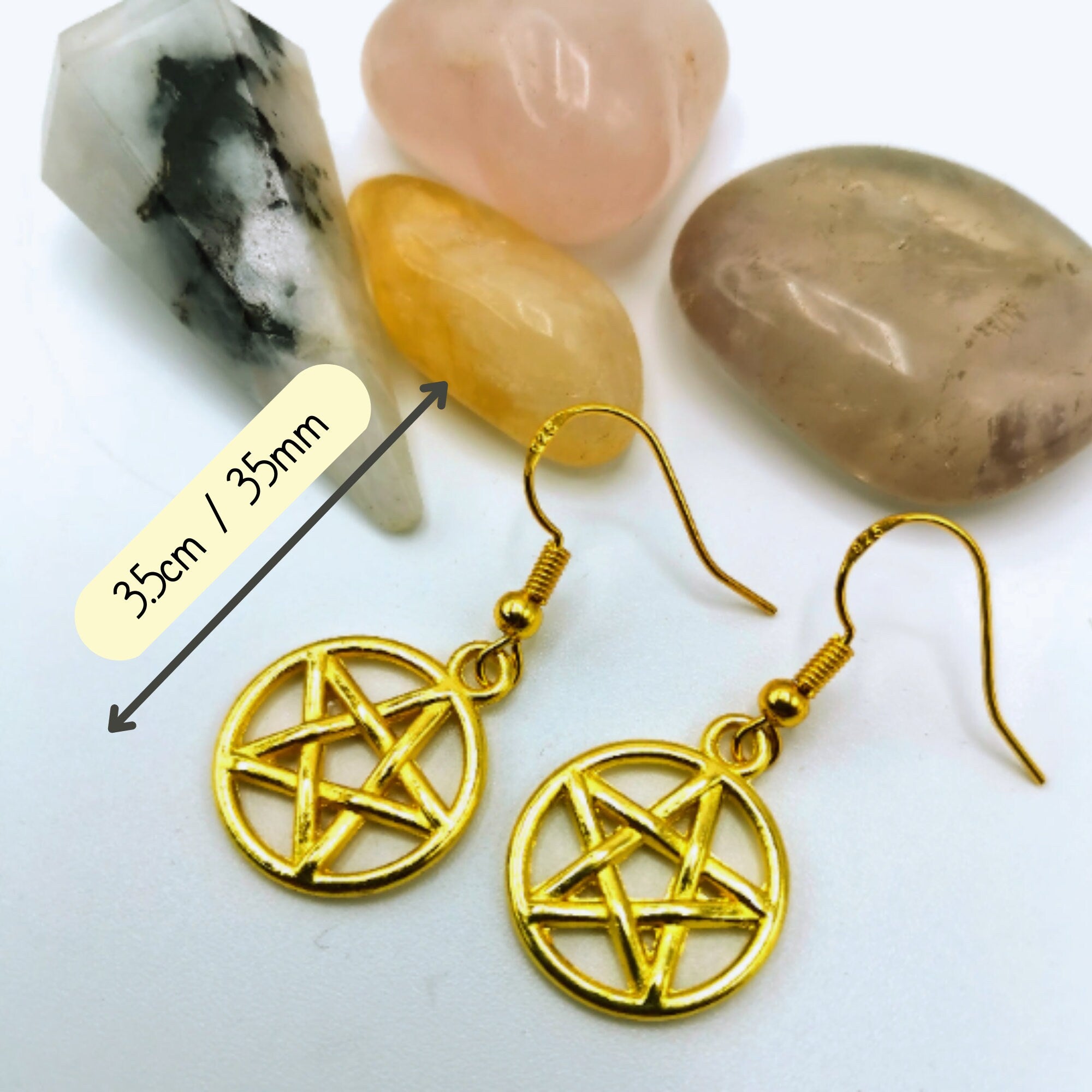 The Silver Sunbird Pentagram Earrings, each 3.5 cm wide and adorned with subtle pagan symbolism, are shown on a white surface beside four polished stones.
