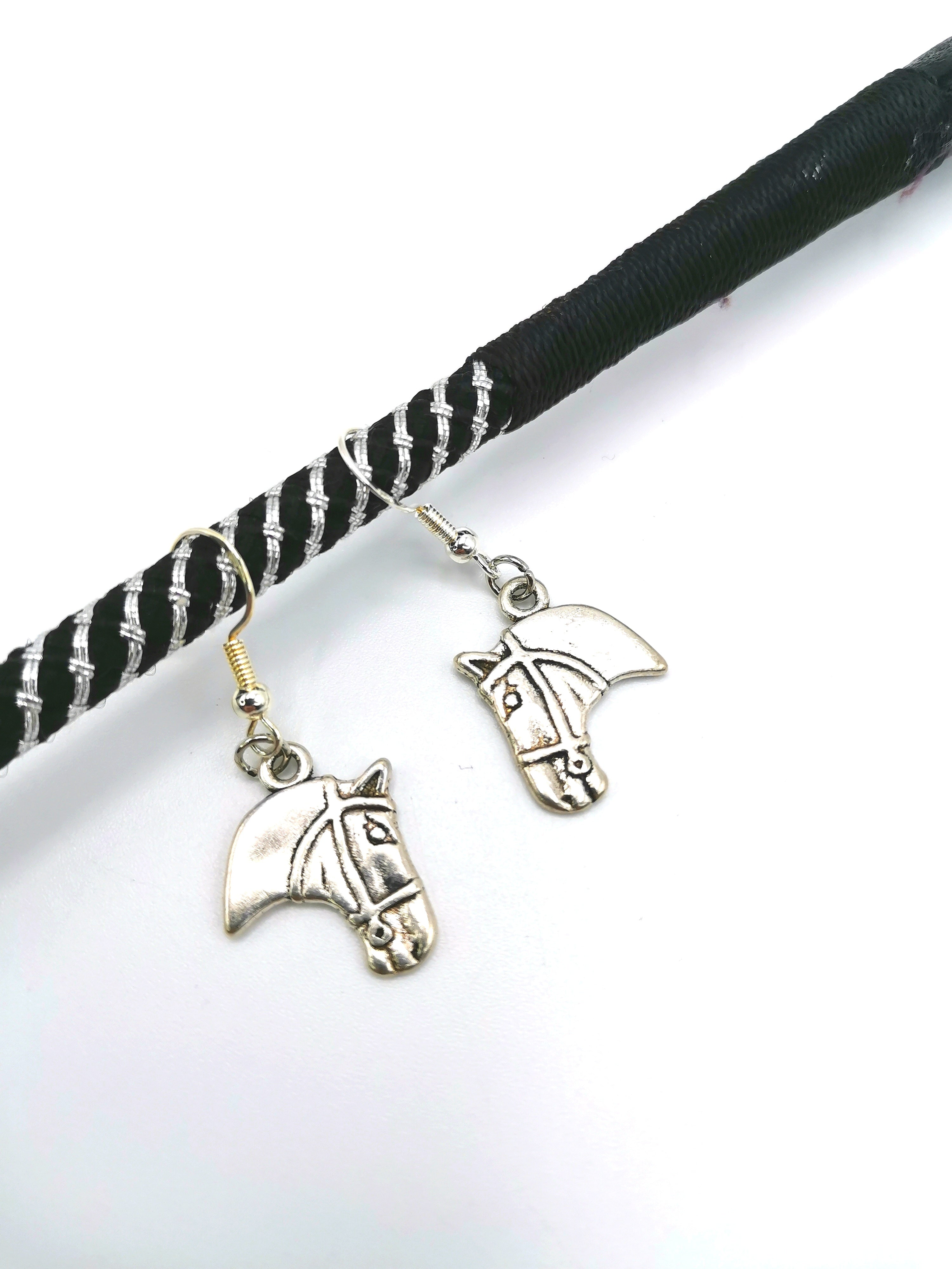 The "Take The Reins Equine Earrings" by Silver Sunbird are sterling silver and hang from a black and white braided string, making them perfect for equestrian jewelry enthusiasts. Each earring showcases a detailed etching of a horse&