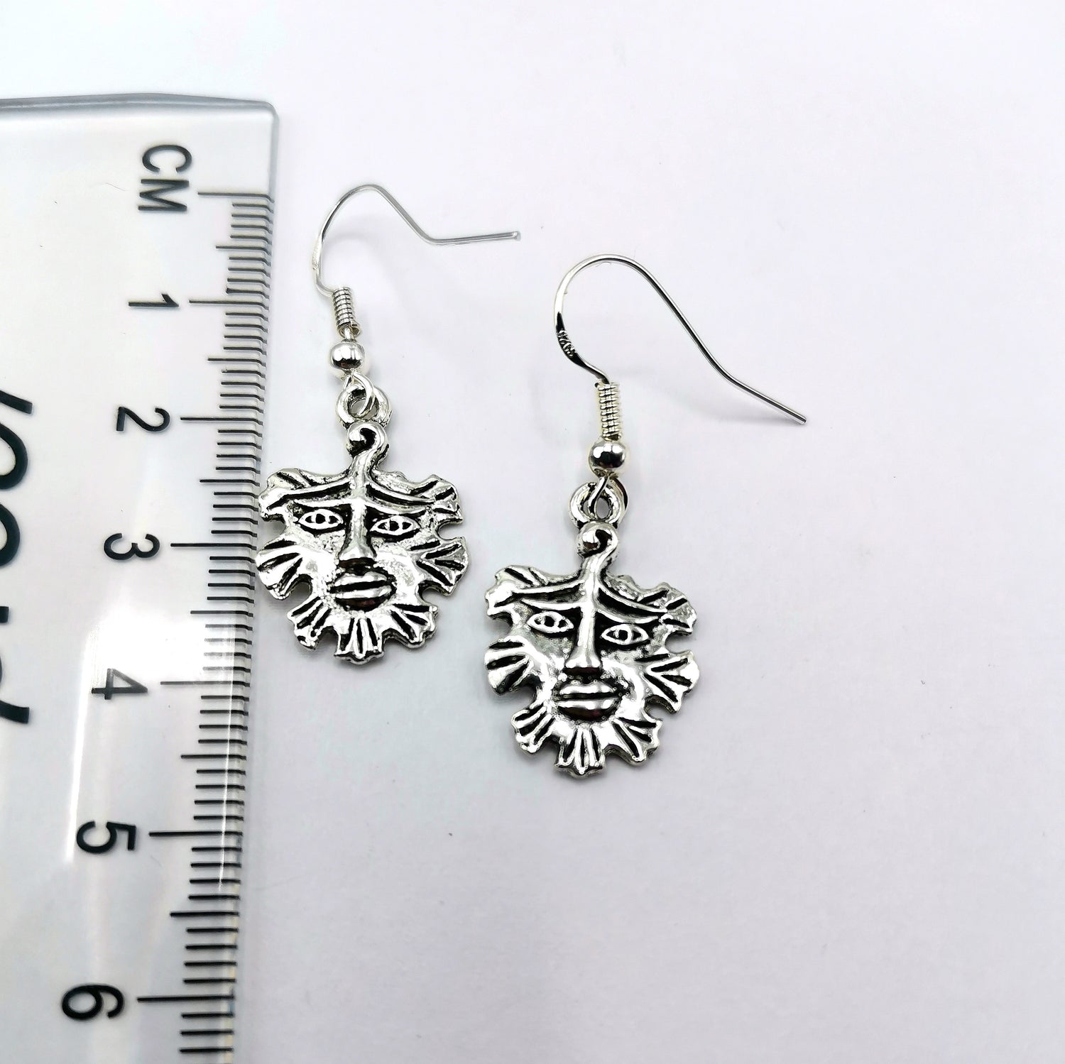 The Gentle Green Man Sterling Silver Earrings by Silver Sunbird, each about 3 cm long with detailed face designs, are shown beside a ruler against a white background—unique pagan-inspired jewellery.