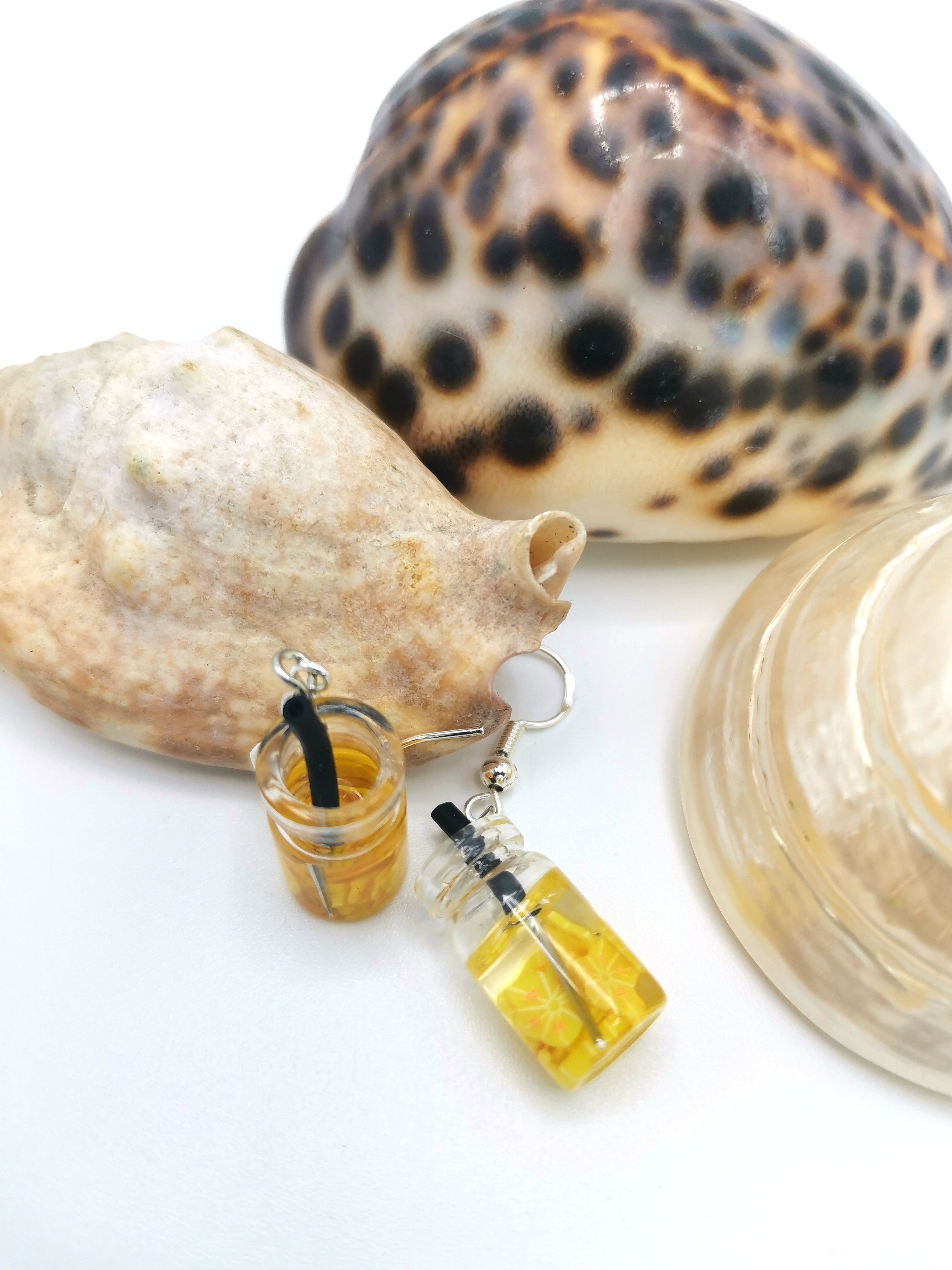 Keychain with mini orange juice bottles and black straws set against large seashells pairs perfectly with Silver Sunbird&