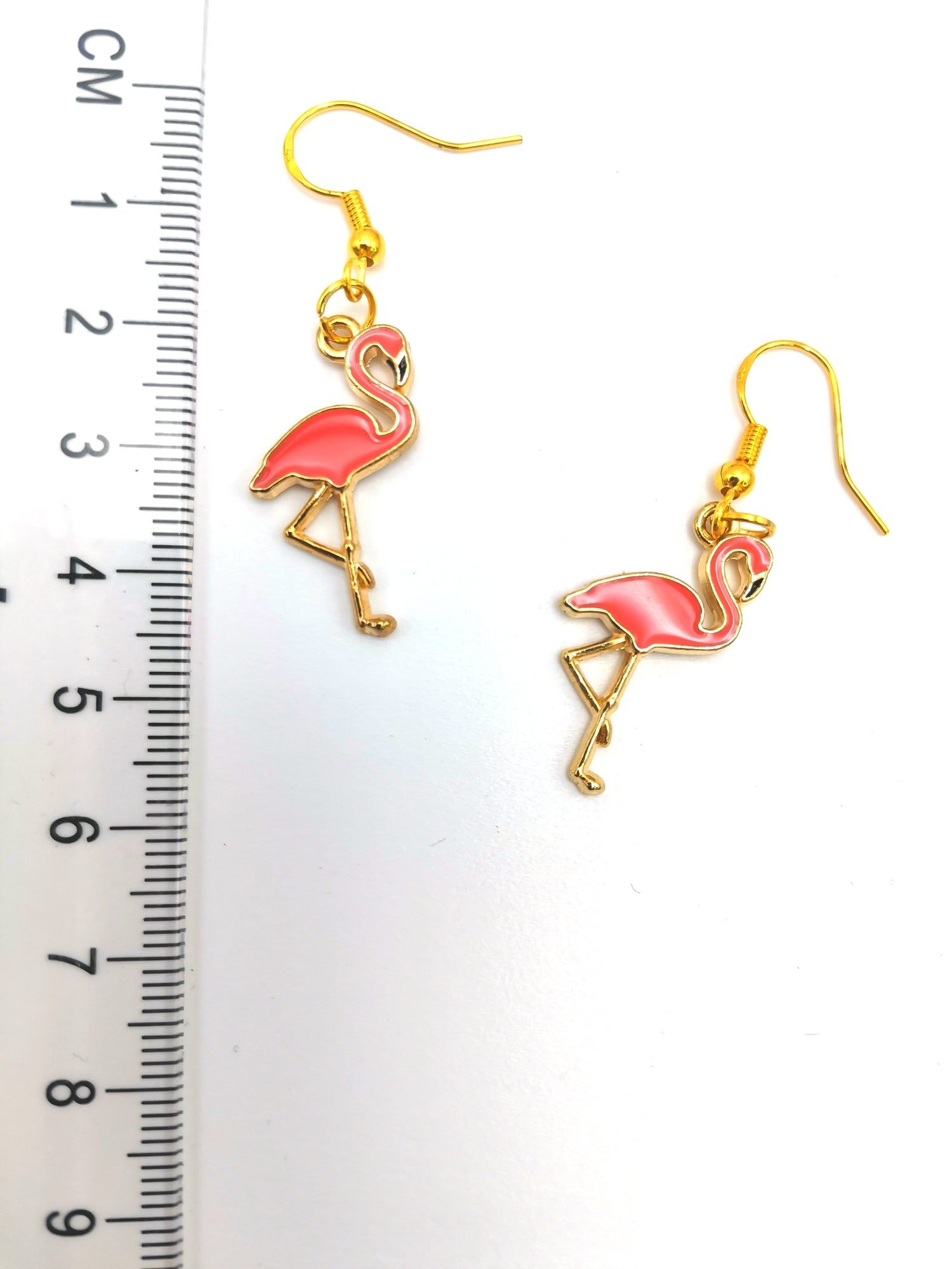 A pair of Dancing Flamingo Earrings by Silver Sunbird with gold-plated sterling silver hooks, placed next to a ruler for size reference. The ruler shows measurements in centimetres, indicating that the handmade jewellery is approximately 4.5 cm long. The background is white.