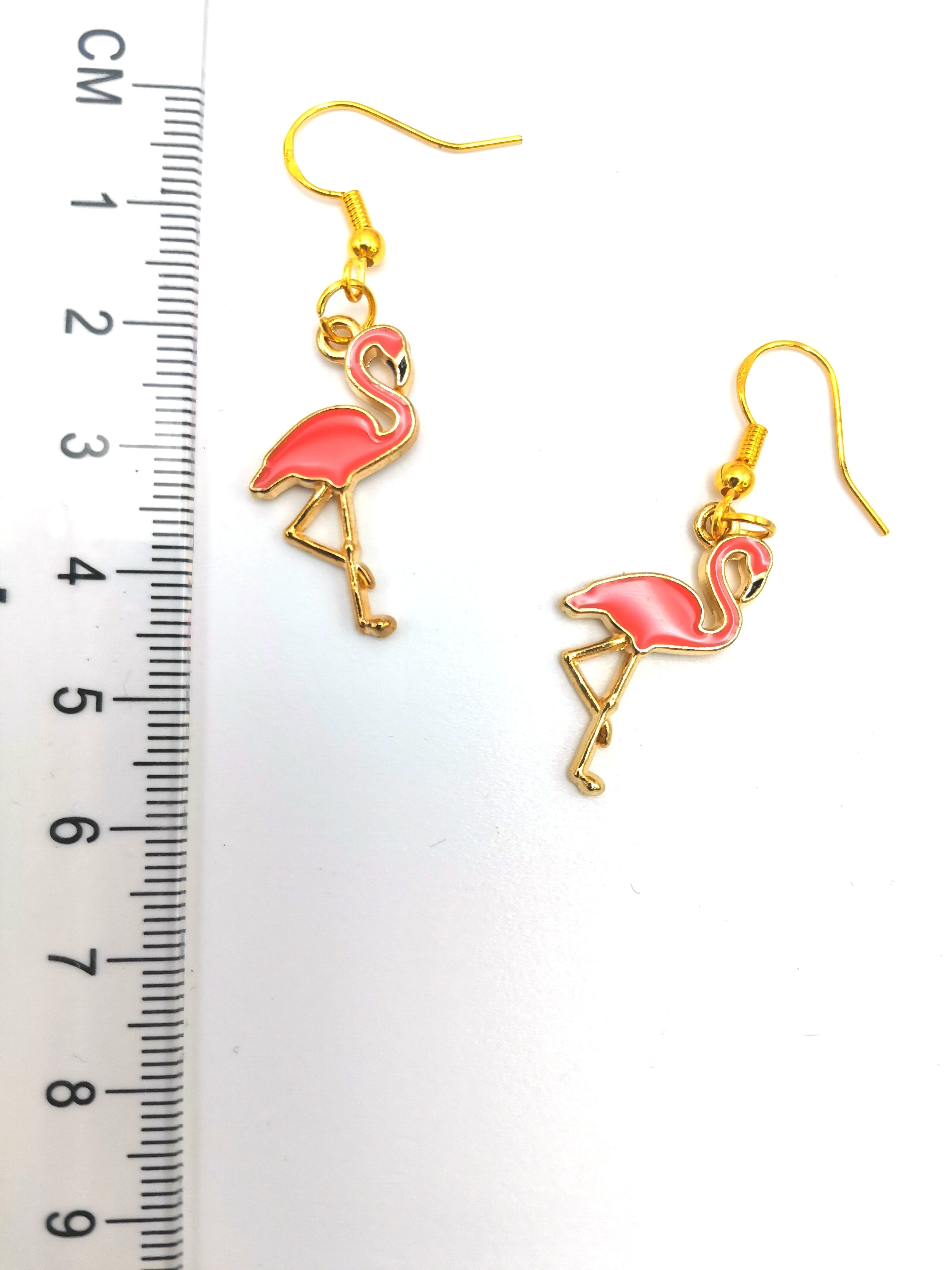 A pair of Dancing Flamingo Earrings by Silver Sunbird with gold-plated sterling silver hooks, placed next to a ruler for size reference. The ruler shows measurements in centimetres, indicating that the handmade jewellery is approximately 4.5 cm long. The background is white.