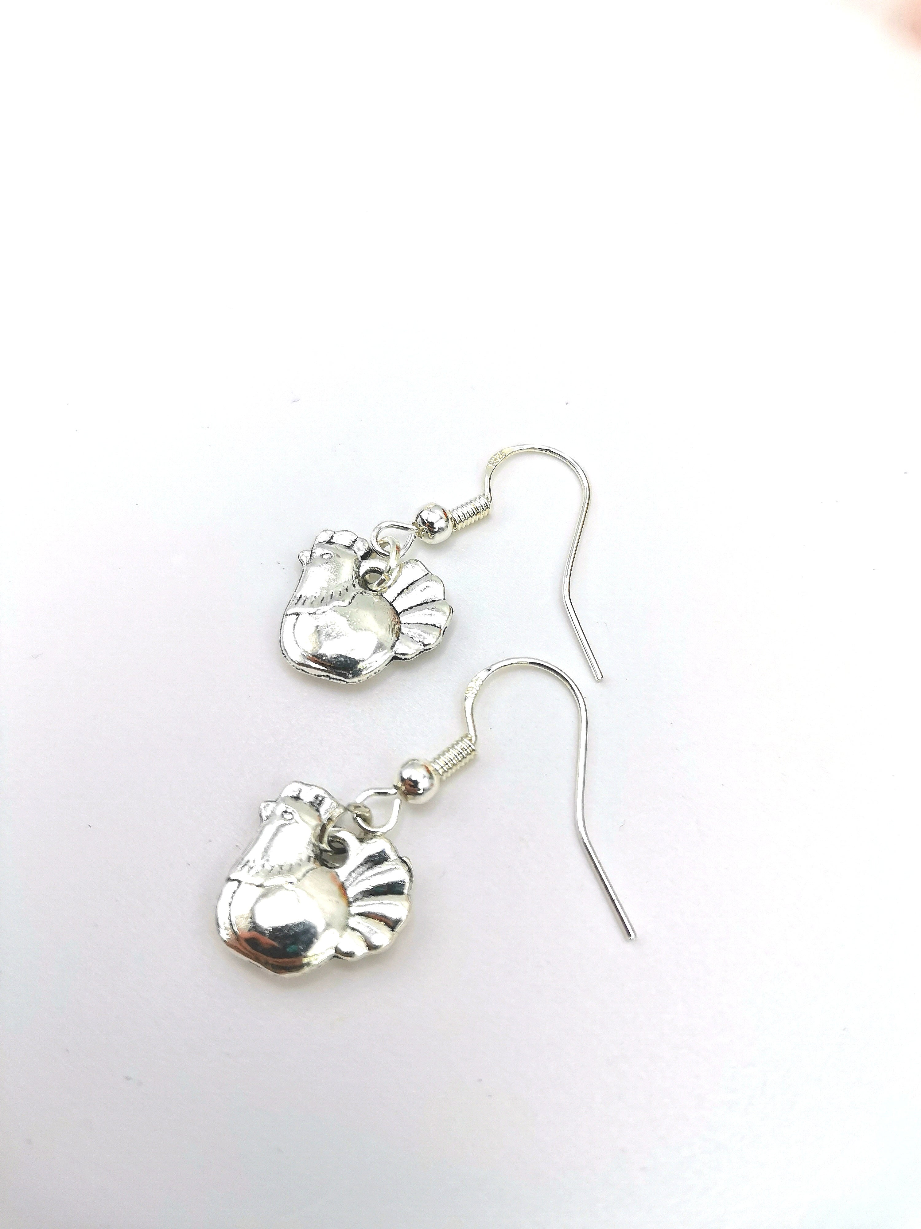 A pair of Charismatic Chicken Earrings by Silver Sunbird, handmade in sterling silver with hen-shaped charms on fishhook wires, showcased on a plain white background.