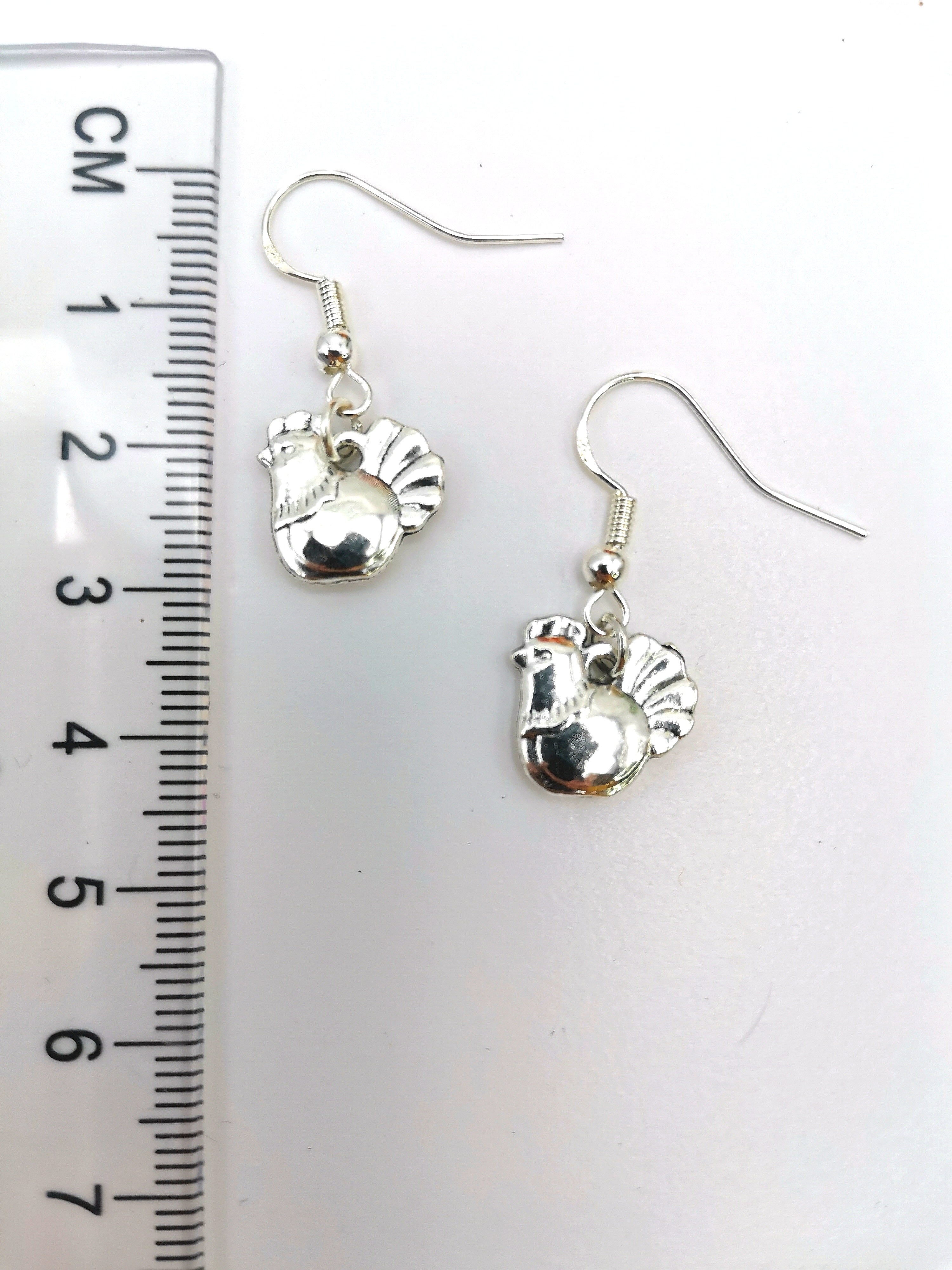 A pair of Charismatic Chicken Earrings by Silver Sunbird, handmade in sterling silver with hen-shaped charms on fishhook wires, showcased on a plain white background.