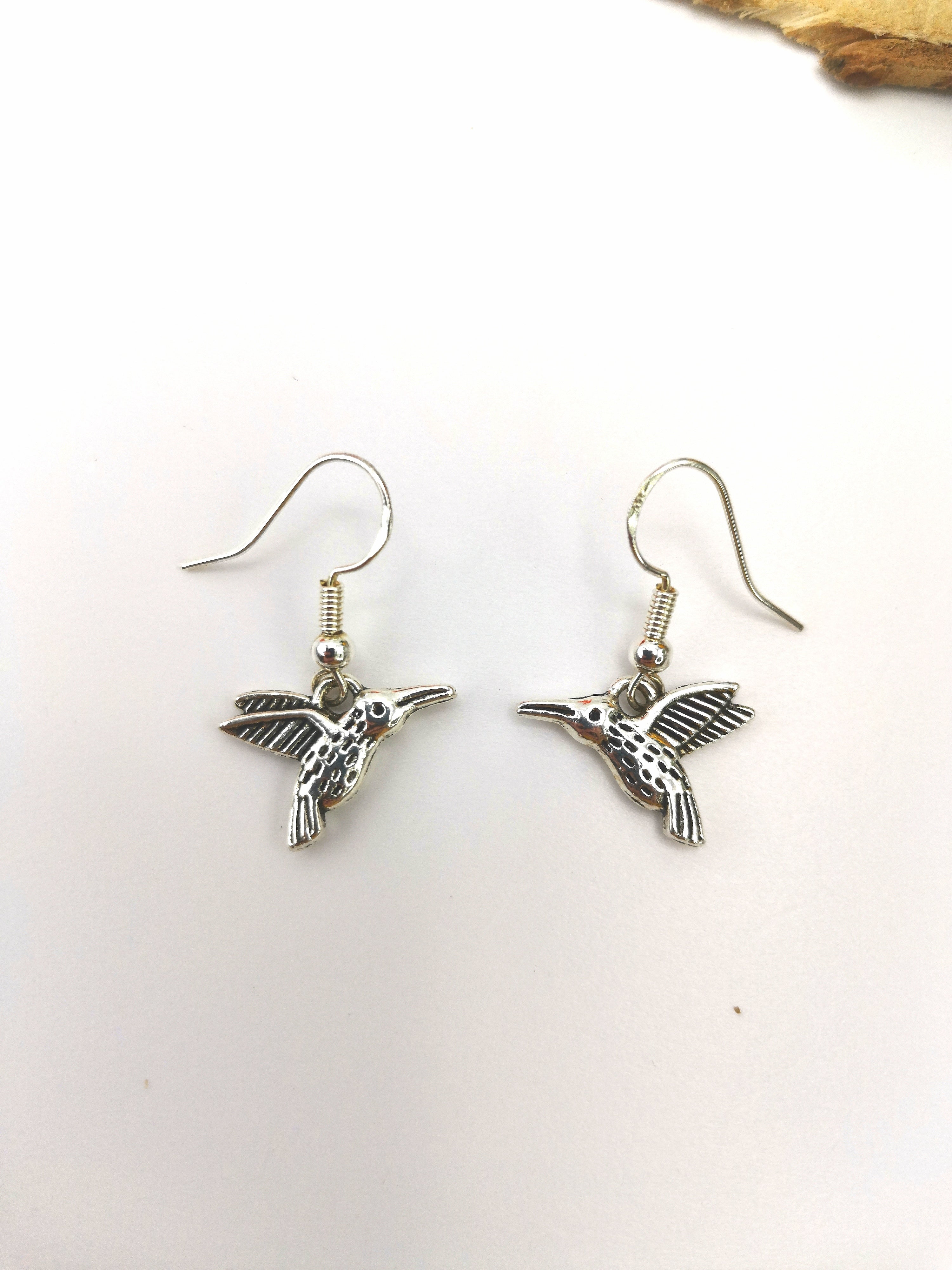 Introducing the Heartfelt Hummingbird Earrings by Silver Sunbird: a pair of sterling silver earrings meticulously crafted in the shape of hummingbirds, featuring detailed wings and bodies. Each bird&