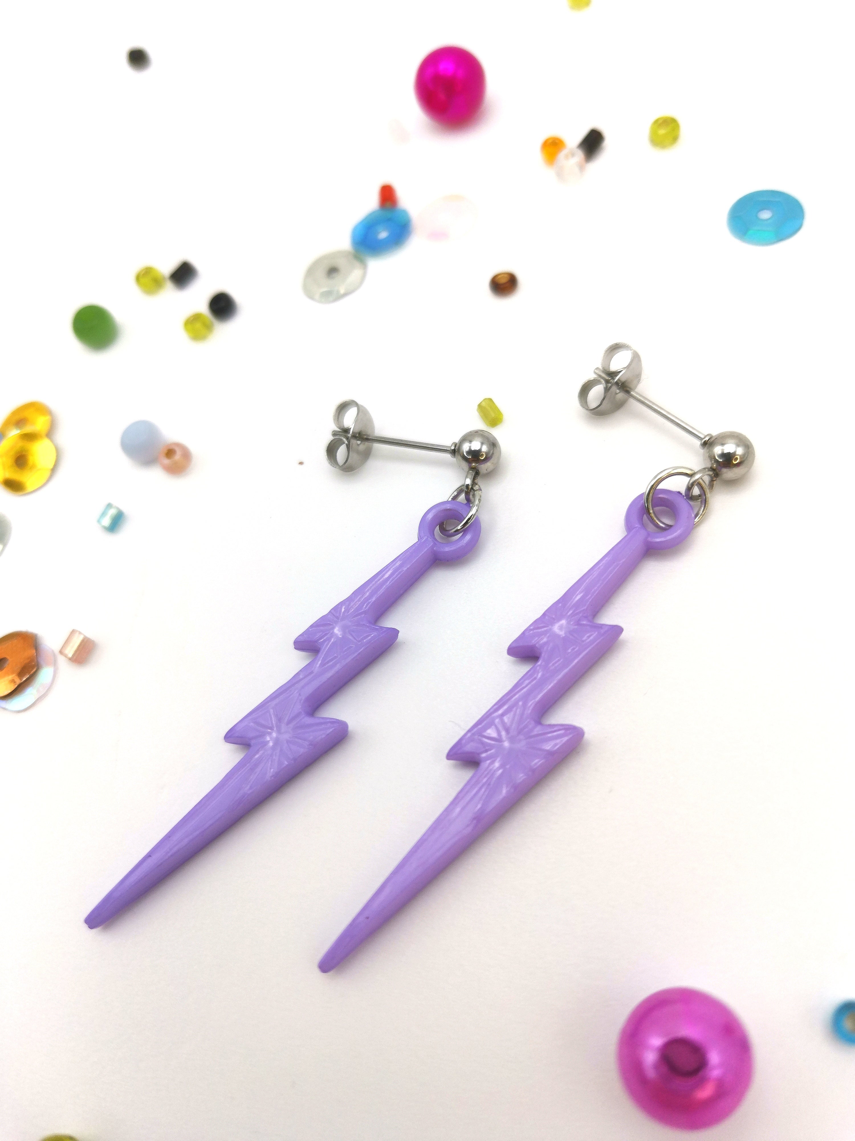 The Electrifying Lightning Bolt Earrings by Silver Sunbird, crafted from hypoallergenic stainless steel with silver studs, are displayed on a white background. Surrounding them are colorful beads and sequins of various shapes and sizes from the vibrant pastel range.