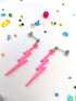The Electrifying Lightning Bolt Earrings from The Pastel Range by Silver Sunbird feature hypoallergenic stainless steel studs, resting on a white surface amidst colorful beads and sequins.