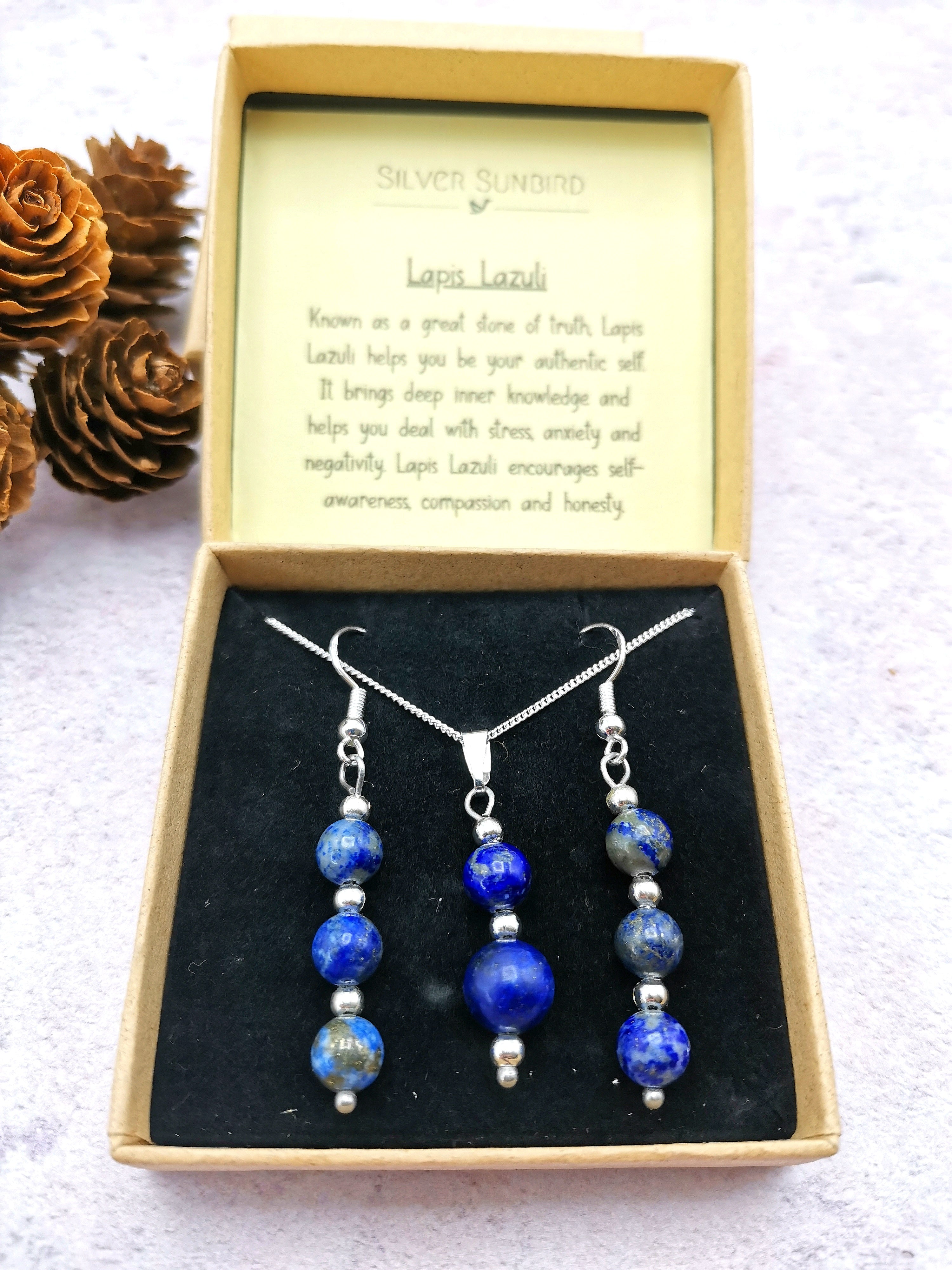 The Silver Sunbird Lapis Lazuli Gemstone Jewellery Set, featuring a 925 sterling silver necklace and earrings, is artfully presented in a box with the stone&