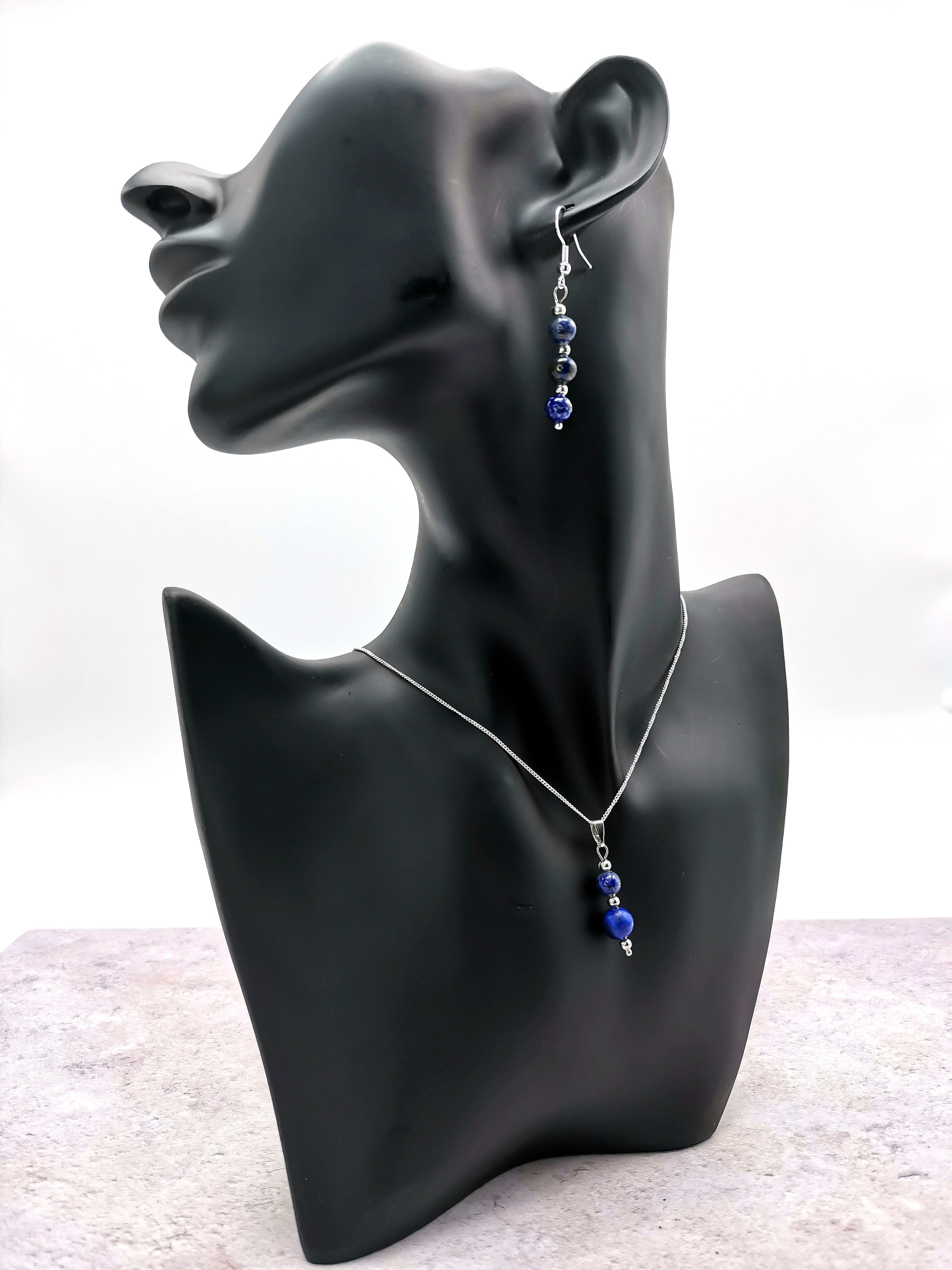 A Silver Sunbird black mannequin bust showcases the Lapis Lazuli Gemstone Jewellery Set in 925 sterling silver, featuring a necklace and earrings with blue beads. The white background contrasts beautifully, highlighting its refined design as an ideal gift set.