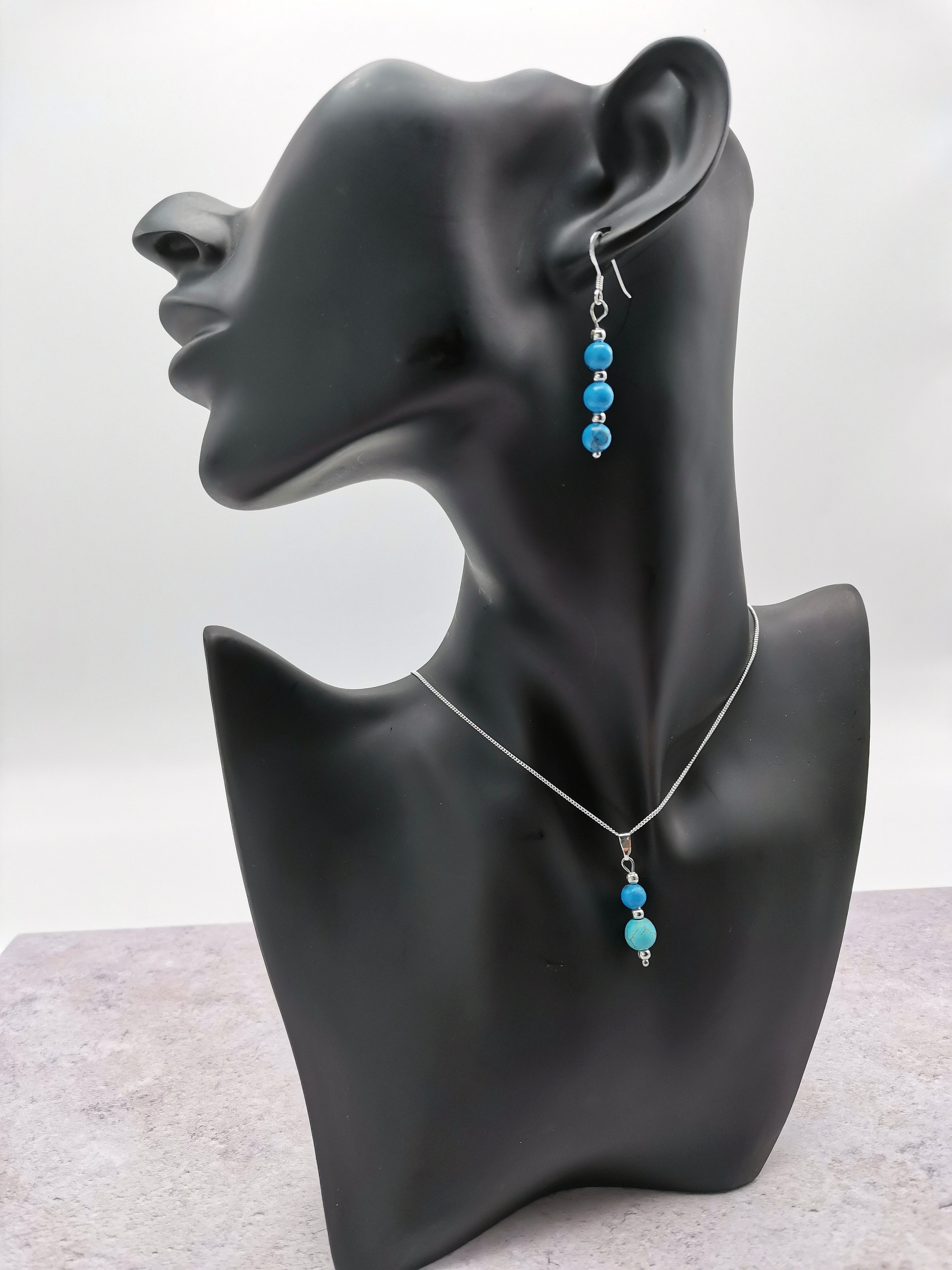 A black mannequin showcases Silver Sunbird’s Turquoise Gemstone Jewellery Set—sterling silver necklace and matching earrings with blue and turquoise beads—against a light gray background.