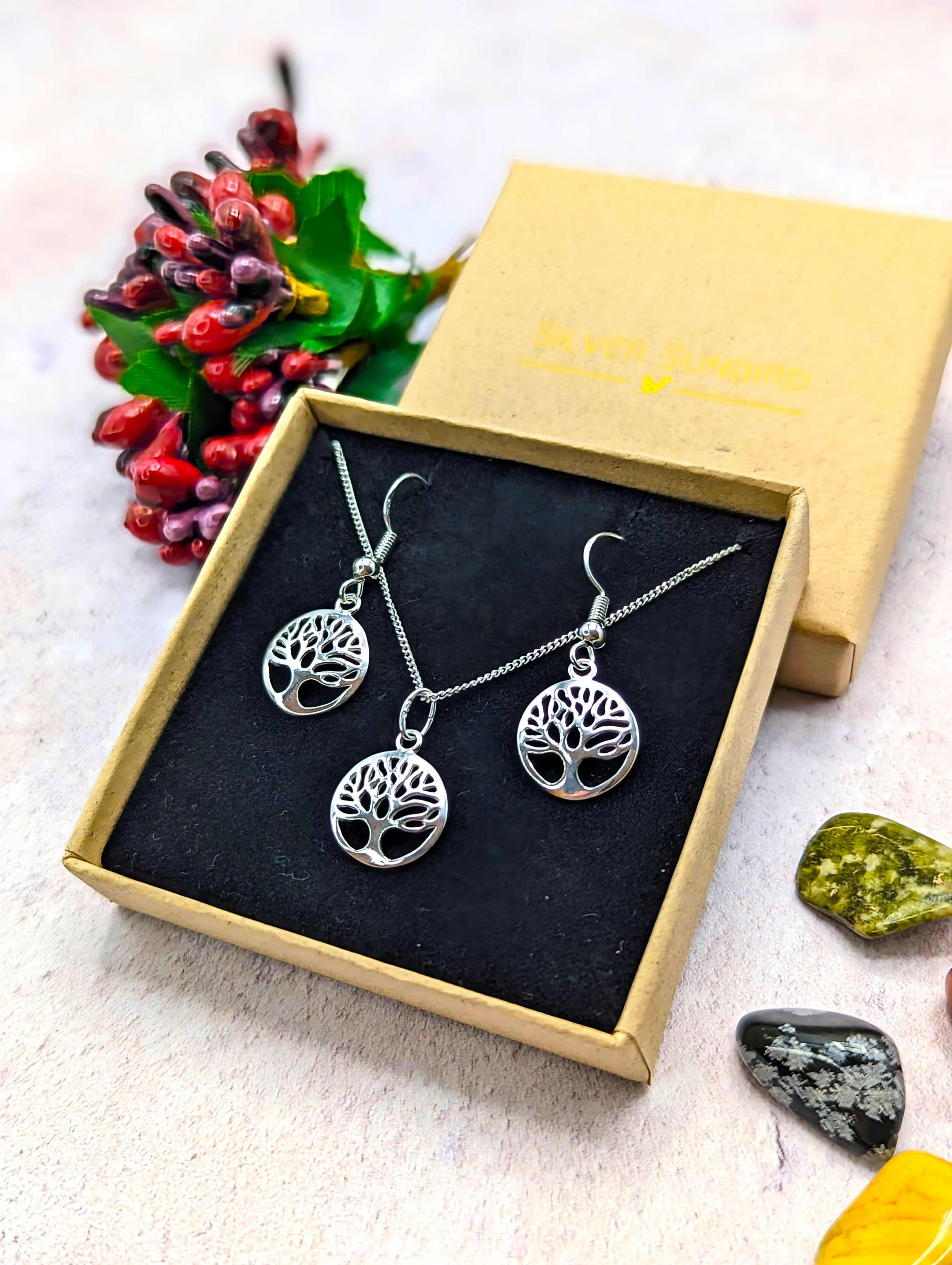 The Sterling Silver Tree of Life Jewellery Set – Necklace & Earrings by Silver Sunbird is presented in a black velvet box, accented with decorative stones and red artificial berries.