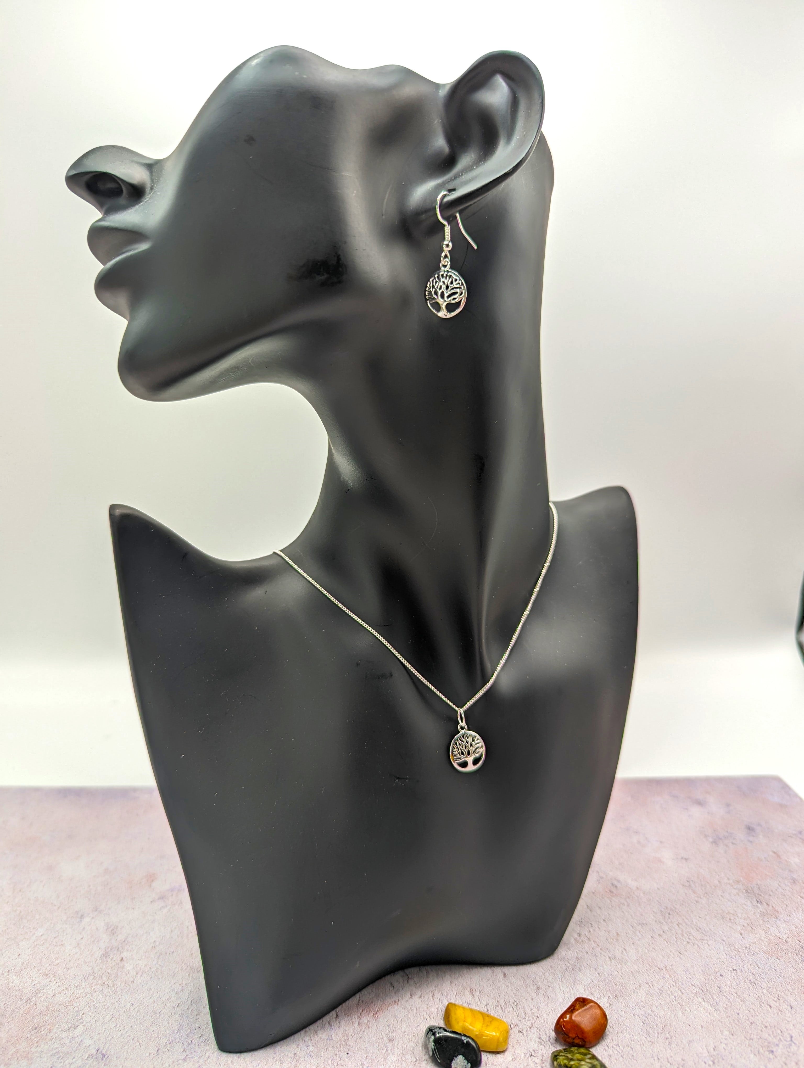 A black mannequin bust displays the Silver Sunbird Sterling Silver Tree of Life Jewellery Set—necklace and hypoallergenic earrings—with three polished stones, on a purple surface.