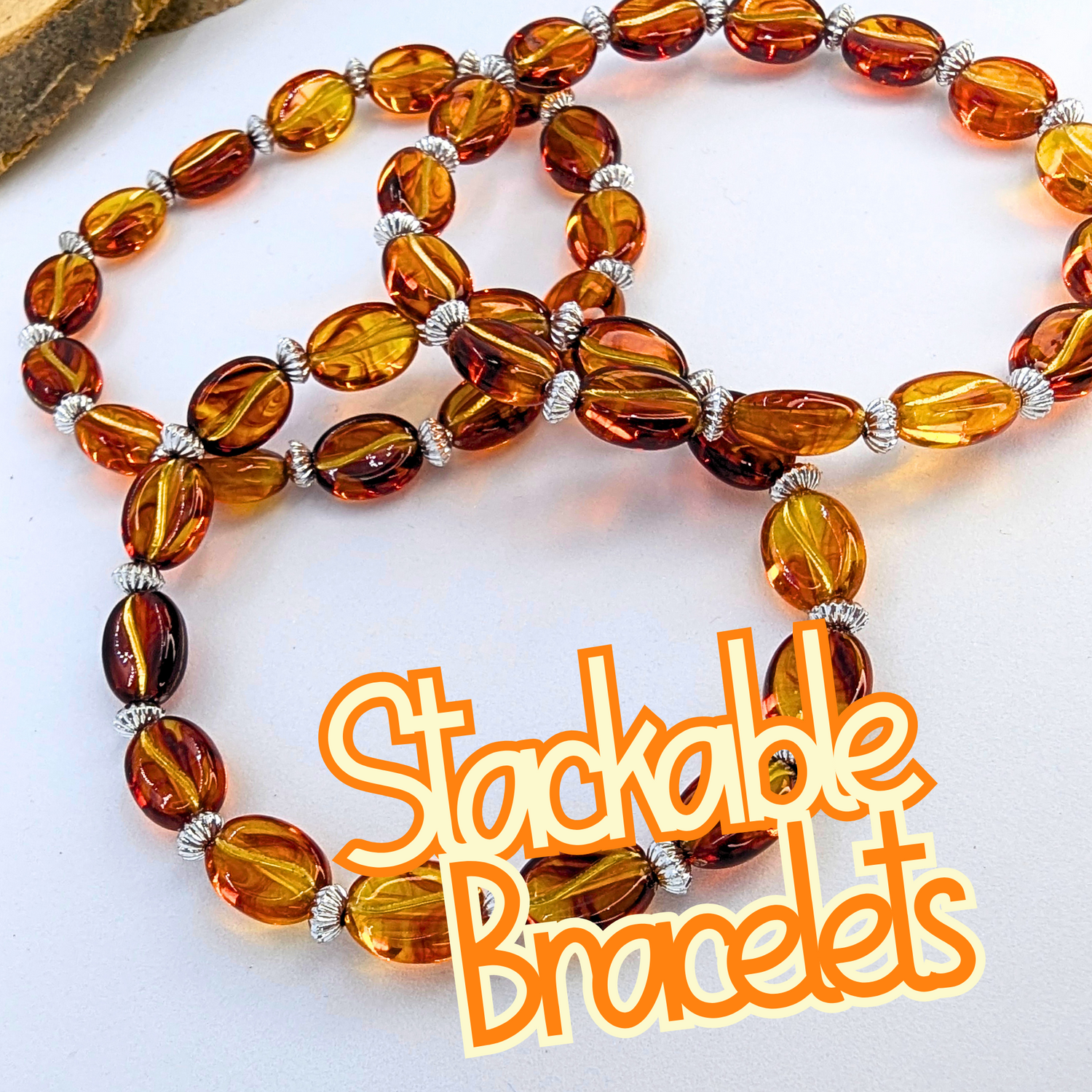 Three stackable bracelets made of amber-colored oval beads and silver spacers are displayed in a spiral shape on a white surface. The words &quot;Stackable Bracelets&quot; are written in orange.