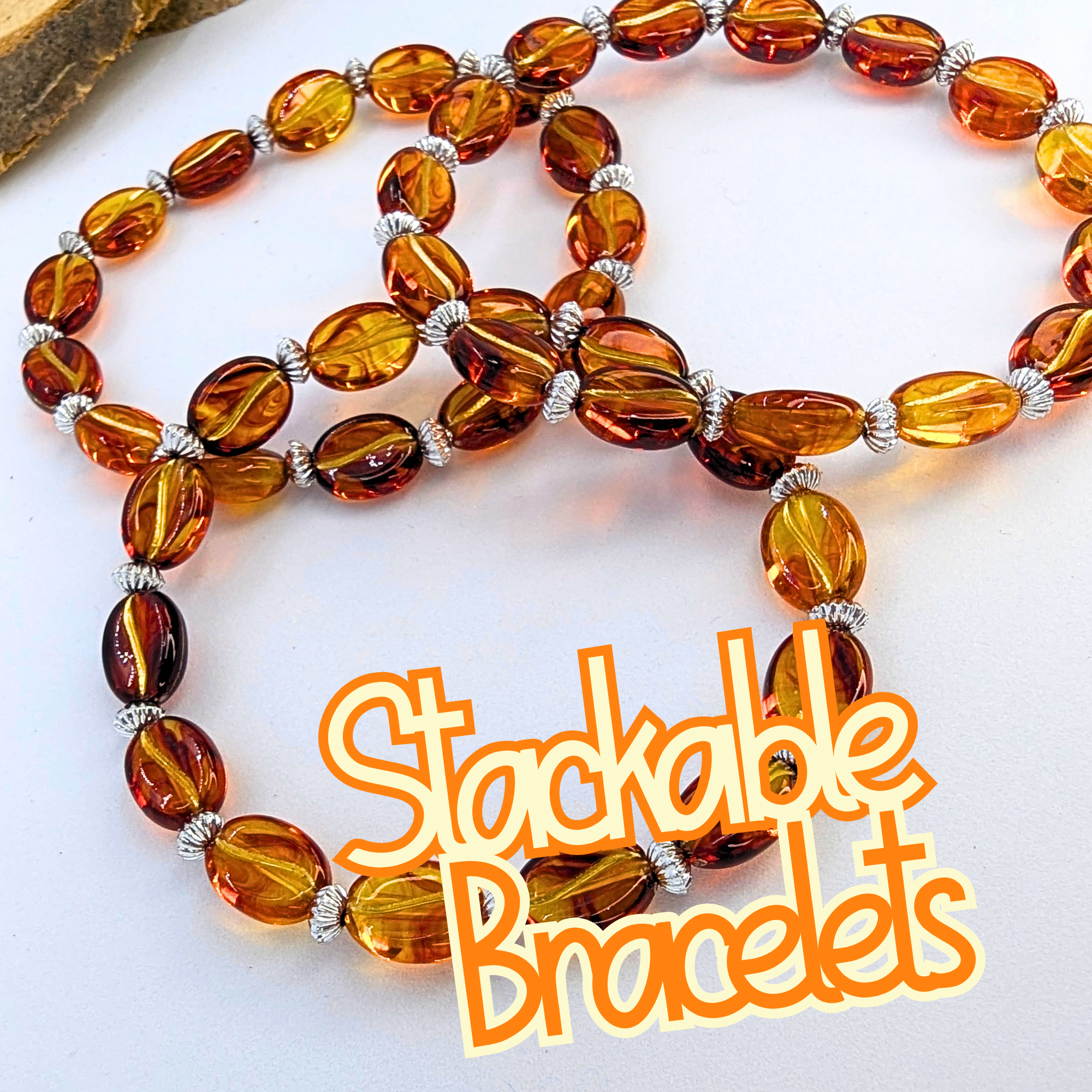 Three stackable bracelets made of amber-colored oval beads and silver spacers are displayed in a spiral shape on a white surface. The words "Stackable Bracelets" are written in orange.