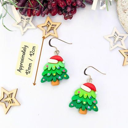 Adorned with vibrant red Santa hats and colorful decorations, the Christmas Tree Earrings by Silver Sunbird make for the perfect holiday accessory. Displayed on a white surface and surrounded by star-shaped wooden decorations, these festive jewelry pieces measure approximately 42mm / 12cm.