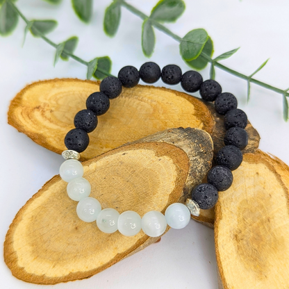 The Silver Sunbird Moonstone and Lava Bracelets are showcased on three overlapping wooden slices, accented with green leaves in the background, all placed on a white surface.