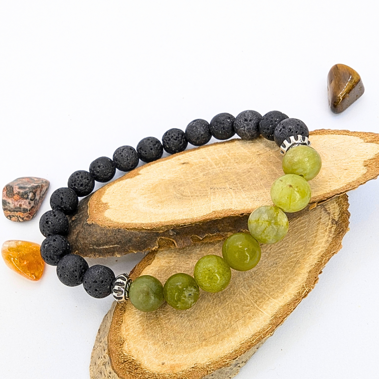 Displayed on slices of wood, the Peridot Bracelet by Silver Sunbird features alternating black and green beads with silver accents, resembling a lava stone bracelet. It&