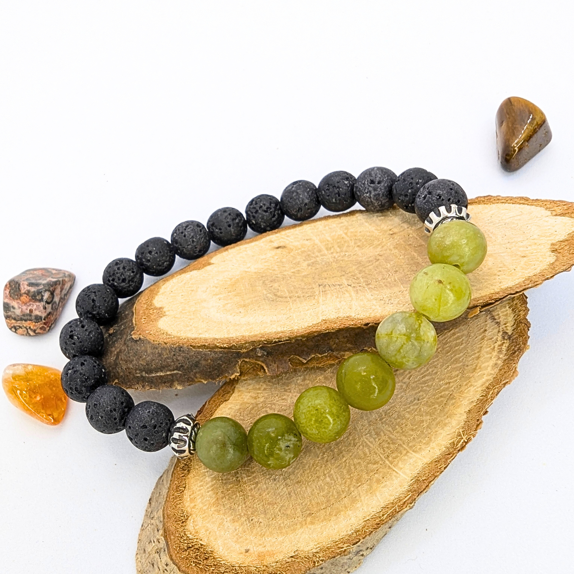 Displayed on slices of wood, the Peridot Bracelet by Silver Sunbird features alternating black and green beads with silver accents, resembling a lava stone bracelet. It&