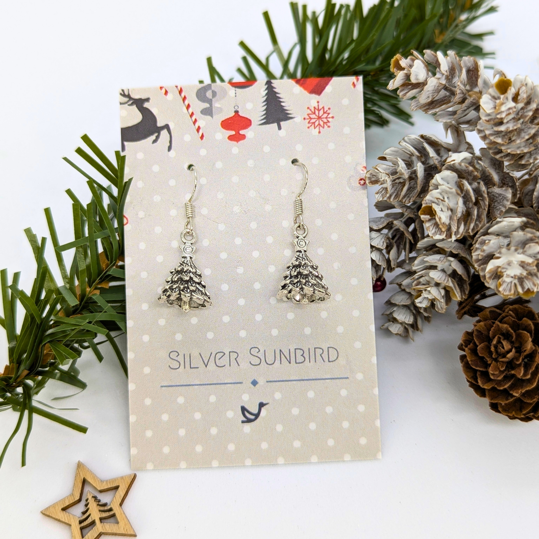 3D Christmas Tree Earrings by Silver Sunbird are displayed on a polka-dot card, surrounded by pinecones, pine branches, and a wooden star ornament.