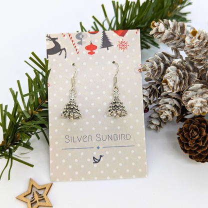 3D Christmas Tree Earrings by Silver Sunbird are displayed on a polka-dot card, surrounded by pinecones, pine branches, and a wooden star ornament.