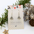 3D Christmas Tree Earrings by Silver Sunbird are displayed on a polka-dot card, surrounded by pinecones, pine branches, and a wooden star ornament.