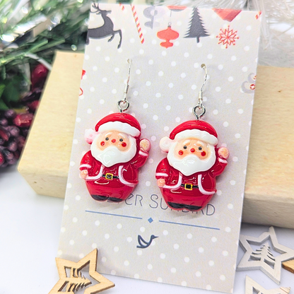 The Jolly Santa Earrings by Silver Sunbird are beautifully showcased on a decorative card with a festive backdrop, highlighting Christmas-themed designs and ornaments. These delightful pieces are ideal Christmas accessories that bring an extra dose of joy to any holiday ensemble.