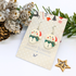Bright Snowmen Earrings by Silver Sunbird feature red hats and green scarves, displayed on a festive card with pinecones, frosted pine branches, and a wooden star—perfect holiday jewelry for Christmas cheer.
