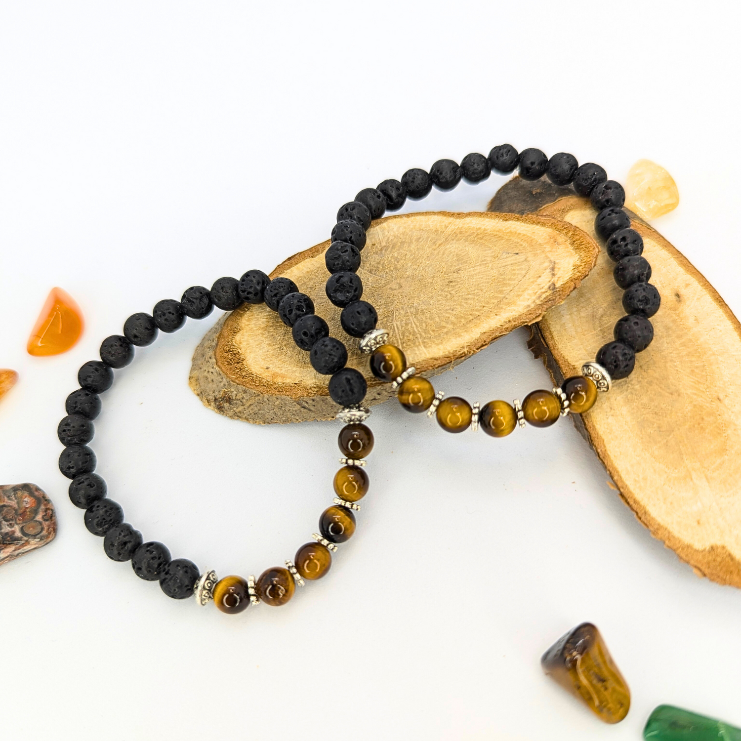 Two beaded bracelets by Silver Sunbird rest on wooden slabs: one with black Lava Stone beads and the other with alternating black and brown Tiger&