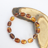 The Silver Sunbird Coffee Bean Bracelet, featuring oval amber beads and silver spacers, is beautifully displayed on two wooden slices atop a white background—ideal for coffee lovers who appreciate unique accessories.