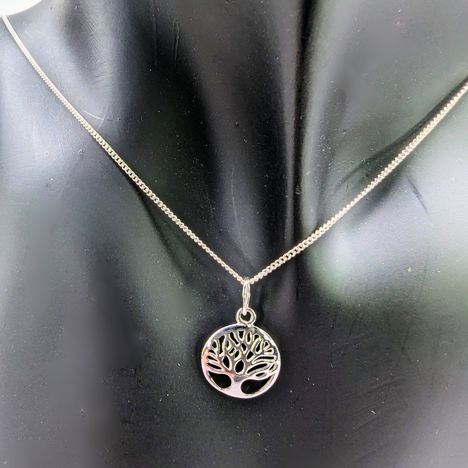 The Silver Sunbird Tree of Life Sterling Silver Necklace, featuring a circular pendant with a cut-out tree design, is displayed on a black mannequin bust as a meaningful jewelry piece.