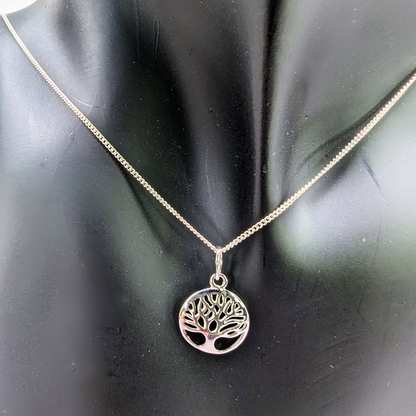 The Silver Sunbird Tree of Life Sterling Silver Necklace, featuring a circular pendant with a cut-out tree design, is displayed on a black mannequin bust as a meaningful jewelry piece.