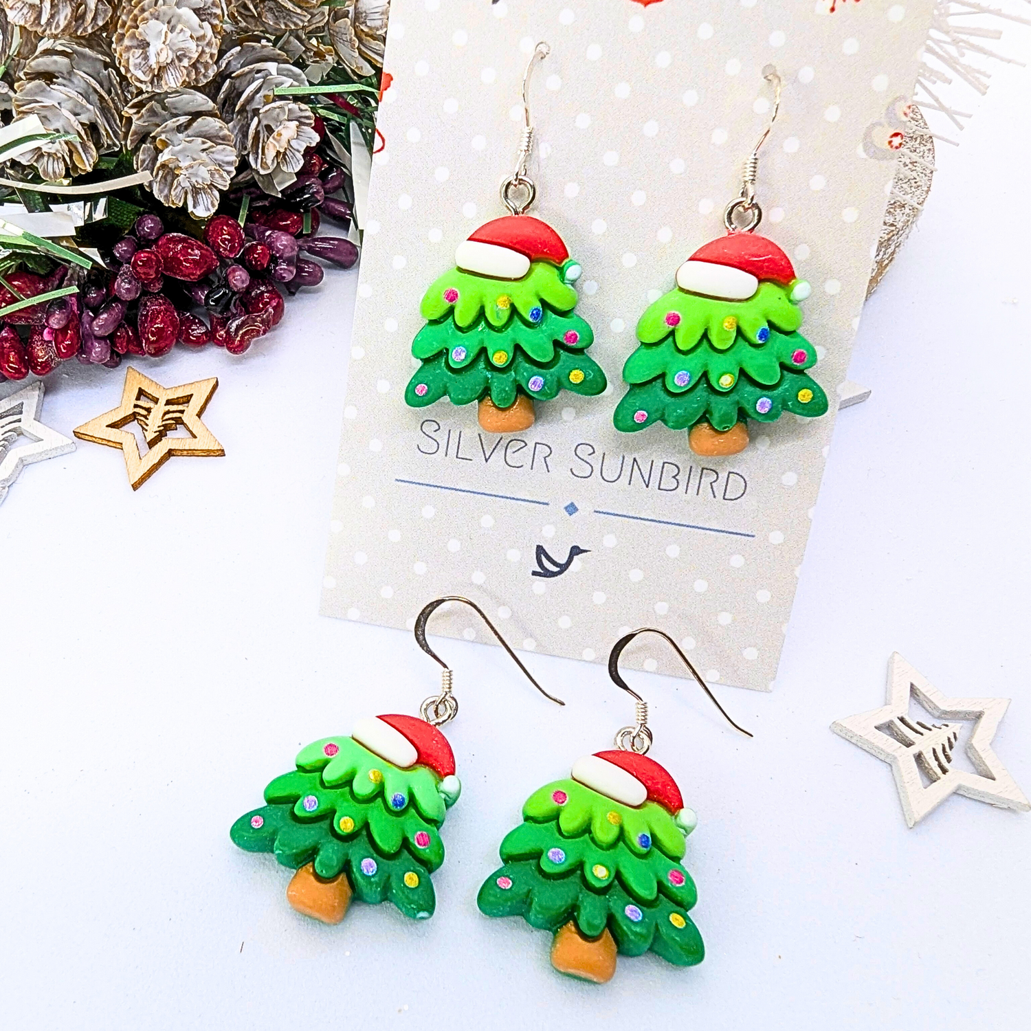 Silver Sunbird presents their charming Christmas Tree Earrings, adorned with Santa hats and displayed against a card bearing the brand&