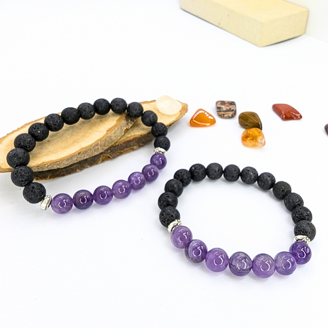 Amethyst and lava stone bracelet with polished purple amethyst beads and textured black lava stones, displayed on a wooden slice with decorative gemstones