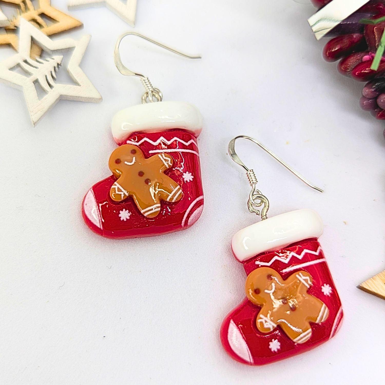 The Gingerbread Men Stocking Earrings by Silver Sunbird are delightful holiday accessories, showcasing red Christmas stockings with white trim and charming gingerbread figures. These earrings are elegantly accented with wooden star decorations and vibrant berries.