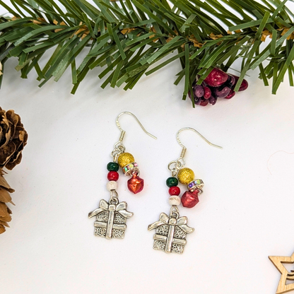 The Silver Sunbird Gift Box Dangle Earrings feature sterling silver hooks and red, green, and gold beads. Displayed with festive pine branches, they make the perfect Christmas accessory!.