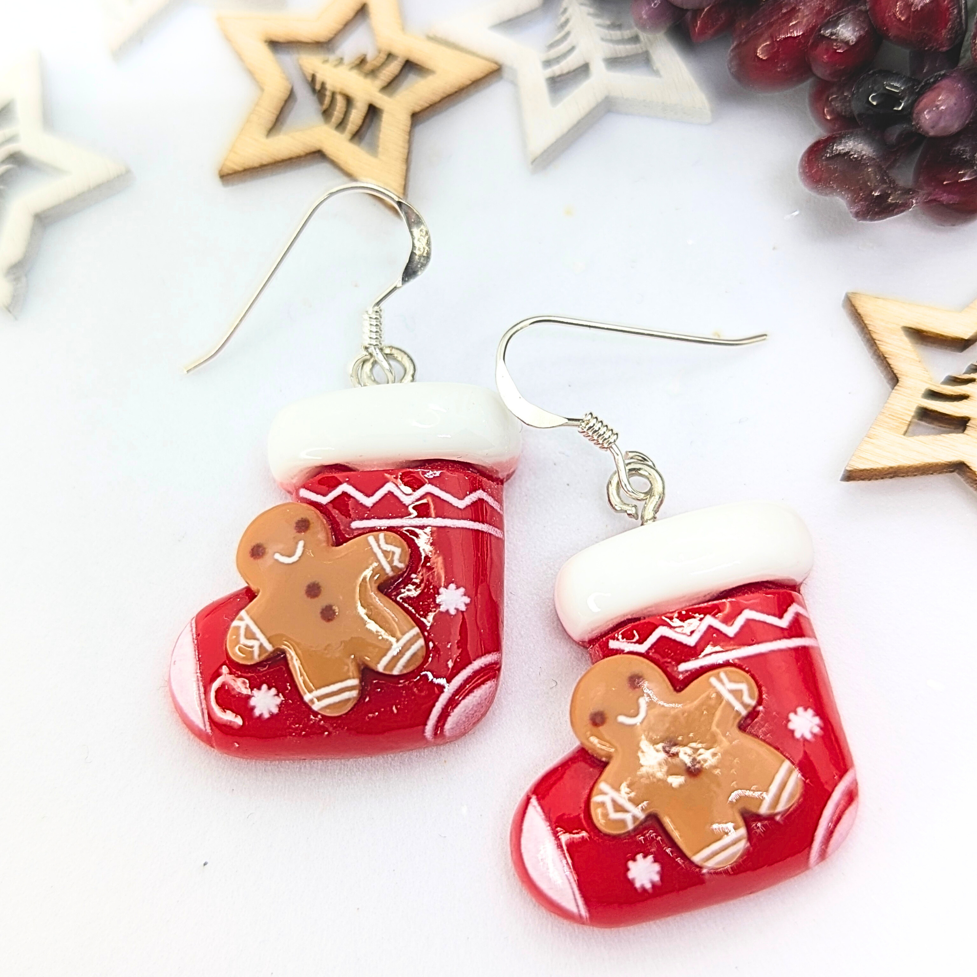 Gingerbread Men Stocking Earrings by Silver Sunbird feature festive Christmas stocking designs with white cuffs, each enhanced by an adorable gingerbread man design. These delightful holiday accessories also showcase wooden star cutouts and red berry accents, making them perfect for adding seasonal cheer to any outfit.