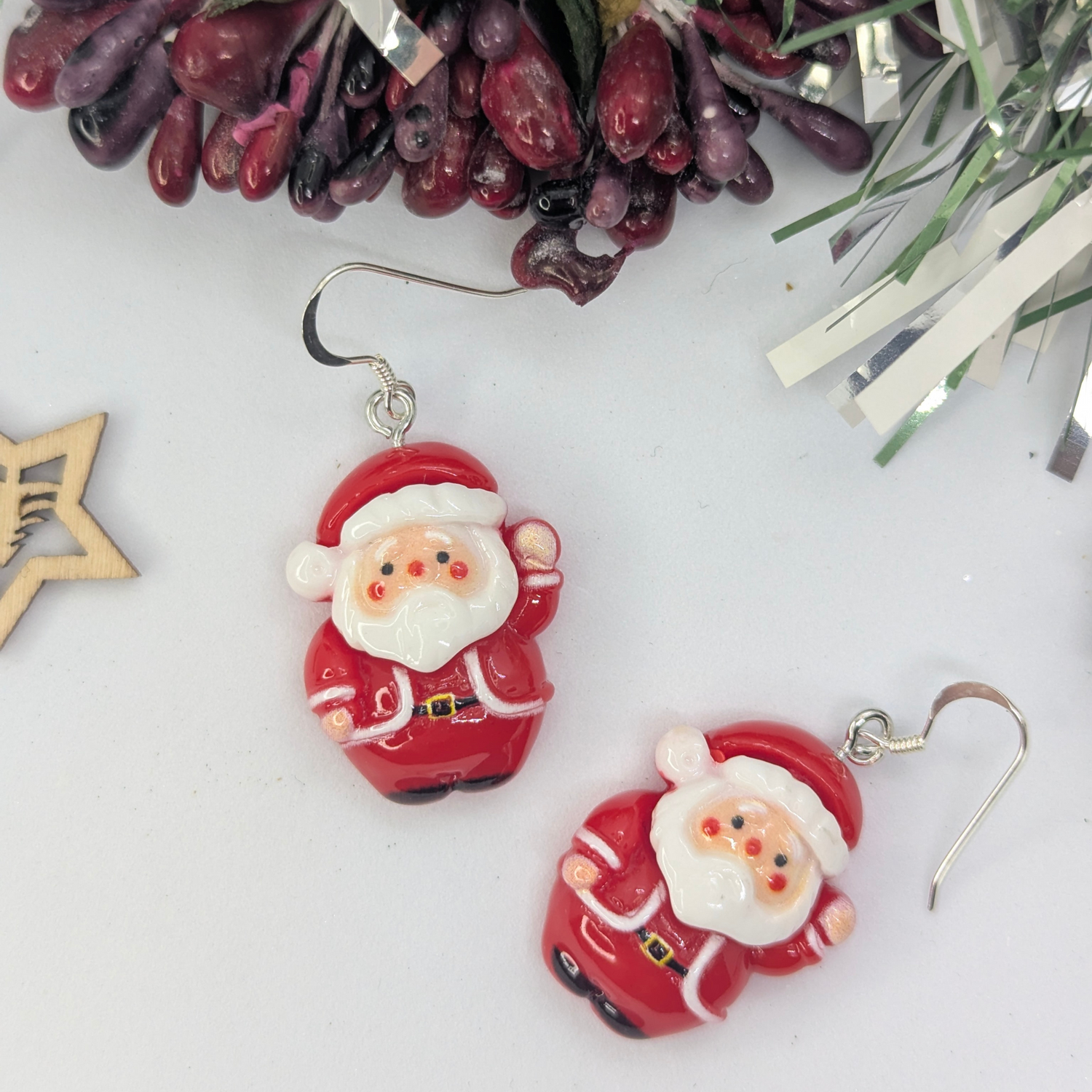 Presenting the Jolly Santa Earrings by Silver Sunbird: a festive set of jewelry pieces that feature cheerful Santa Claus designs. These earrings perfectly capture the spirit of Christmas with delightful holiday decorations, including berries and a wooden star cutout in the background.