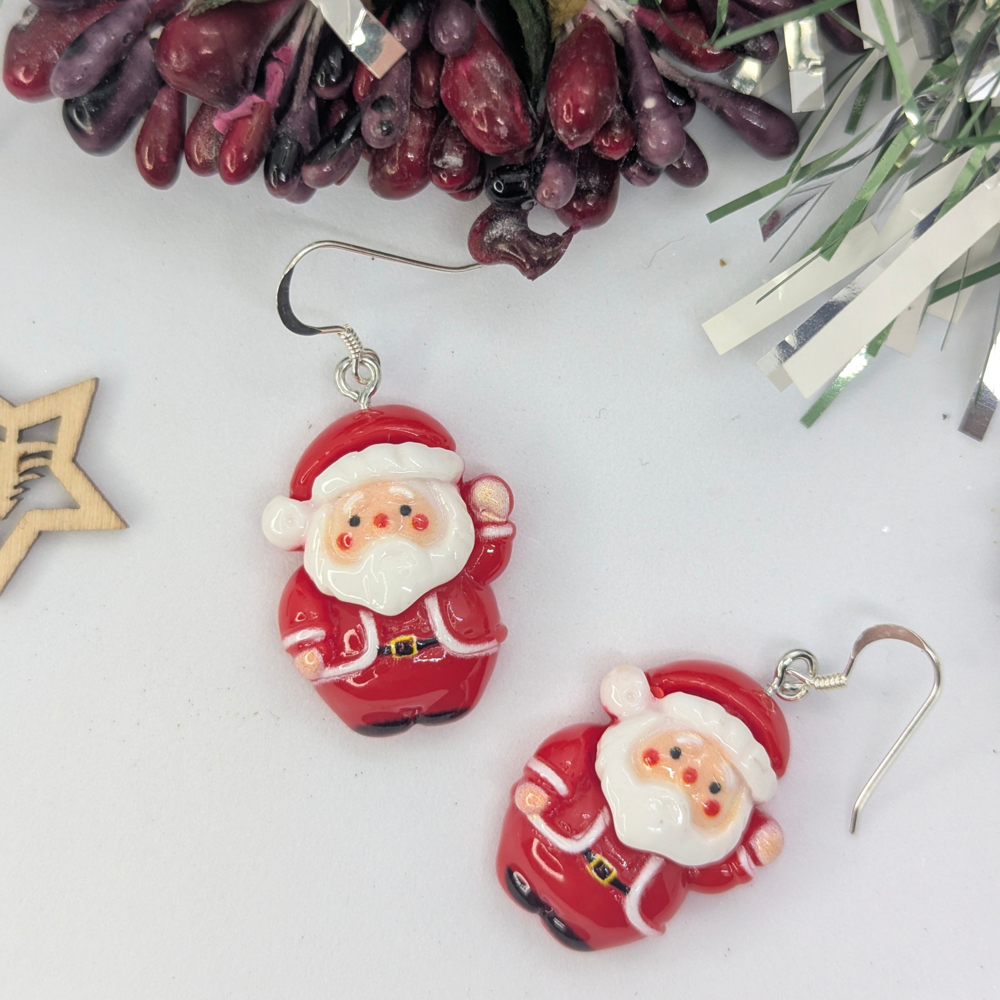 Presenting the Jolly Santa Earrings by Silver Sunbird: a festive set of jewelry pieces that feature cheerful Santa Claus designs. These earrings perfectly capture the spirit of Christmas with delightful holiday decorations, including berries and a wooden star cutout in the background.