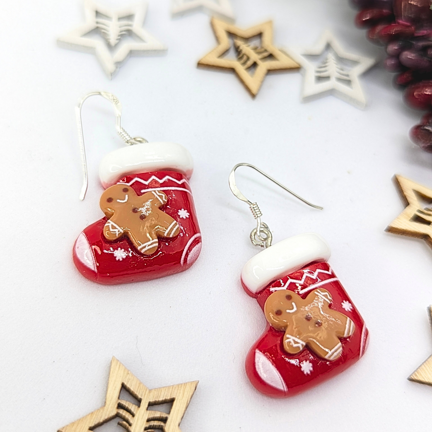 The Gingerbread Men Stocking Earrings by Silver Sunbird are festive holiday accessories shaped like red stockings with charming gingerbread men, surrounded by wooden star designs. These Christmas earrings boast white cuffs and intricate snowflake details, perfectly embodying a delightful Christmas theme.