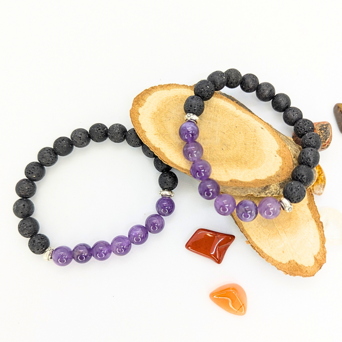 Amethyst and lava stone bracelet with polished purple amethyst beads and textured black lava stones, displayed on a wooden slice with decorative gemstones